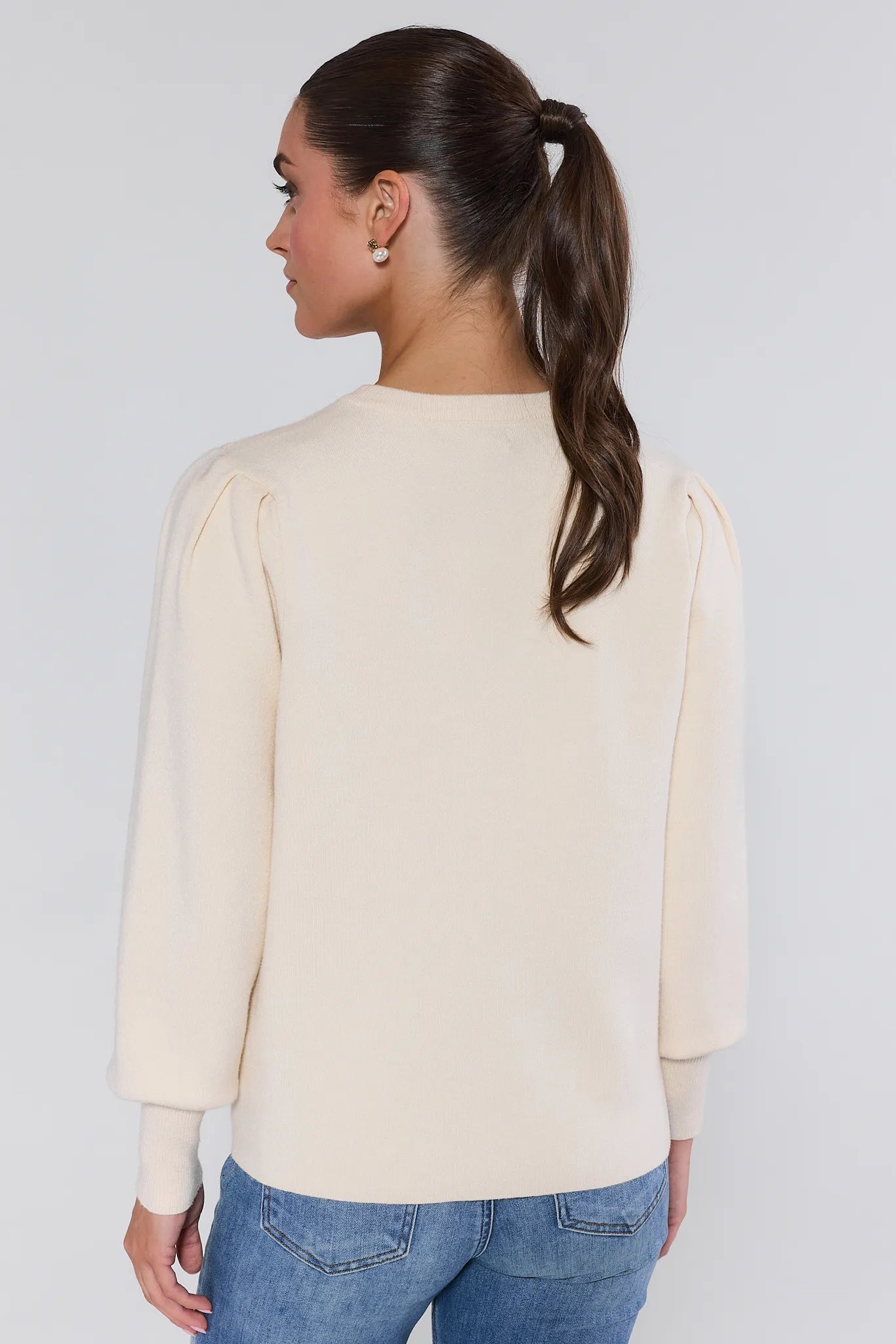 Woman wearing a beige merry sweater and blue jeans against a plain background