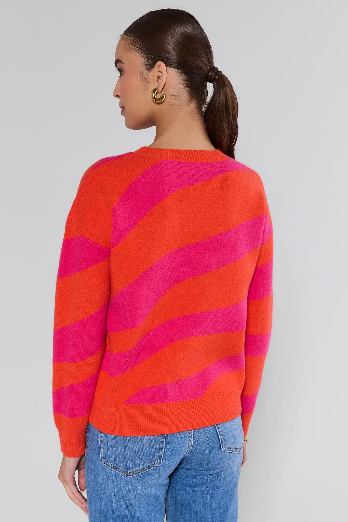 Person wearing a red and pink striped sweater with blue jeans on a plain background