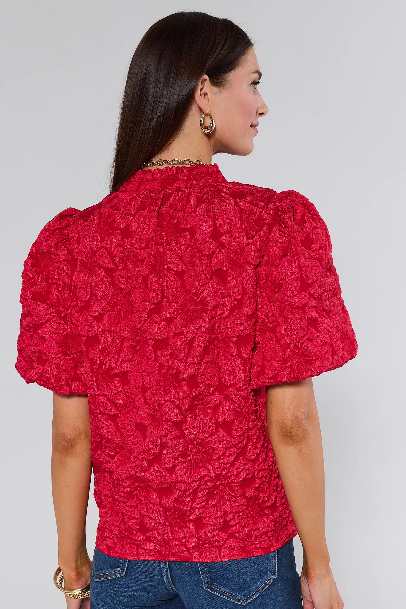 Woman wearing a red textured Teresa Floral Top with blue jeans on a white background