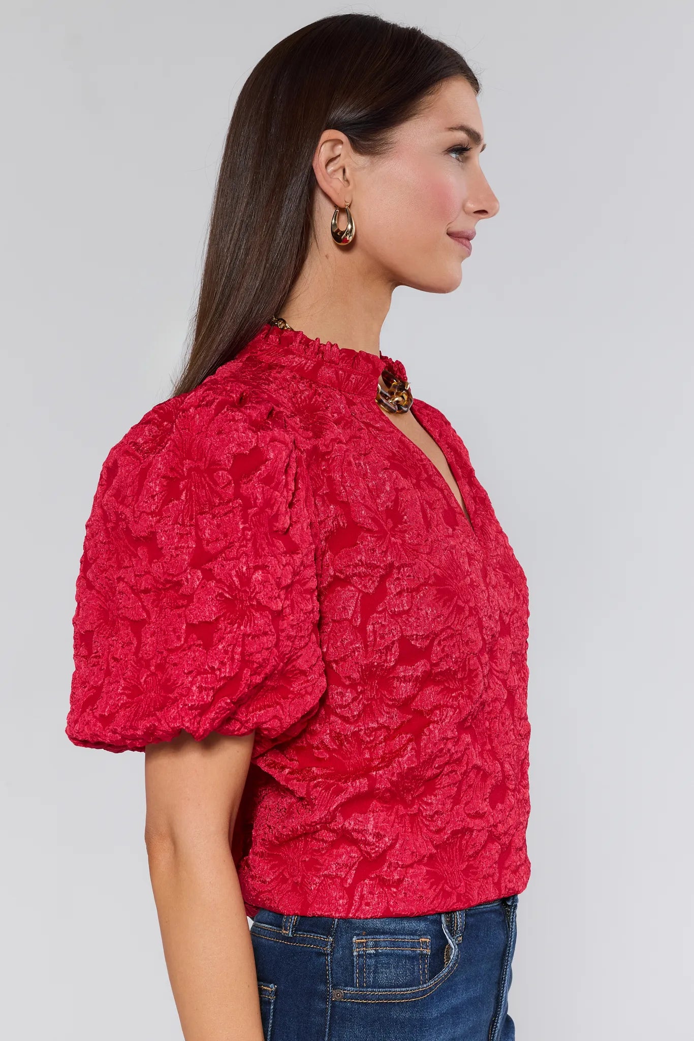 Woman wearing a red textured Teresa Floral Top with blue jeans on a white background