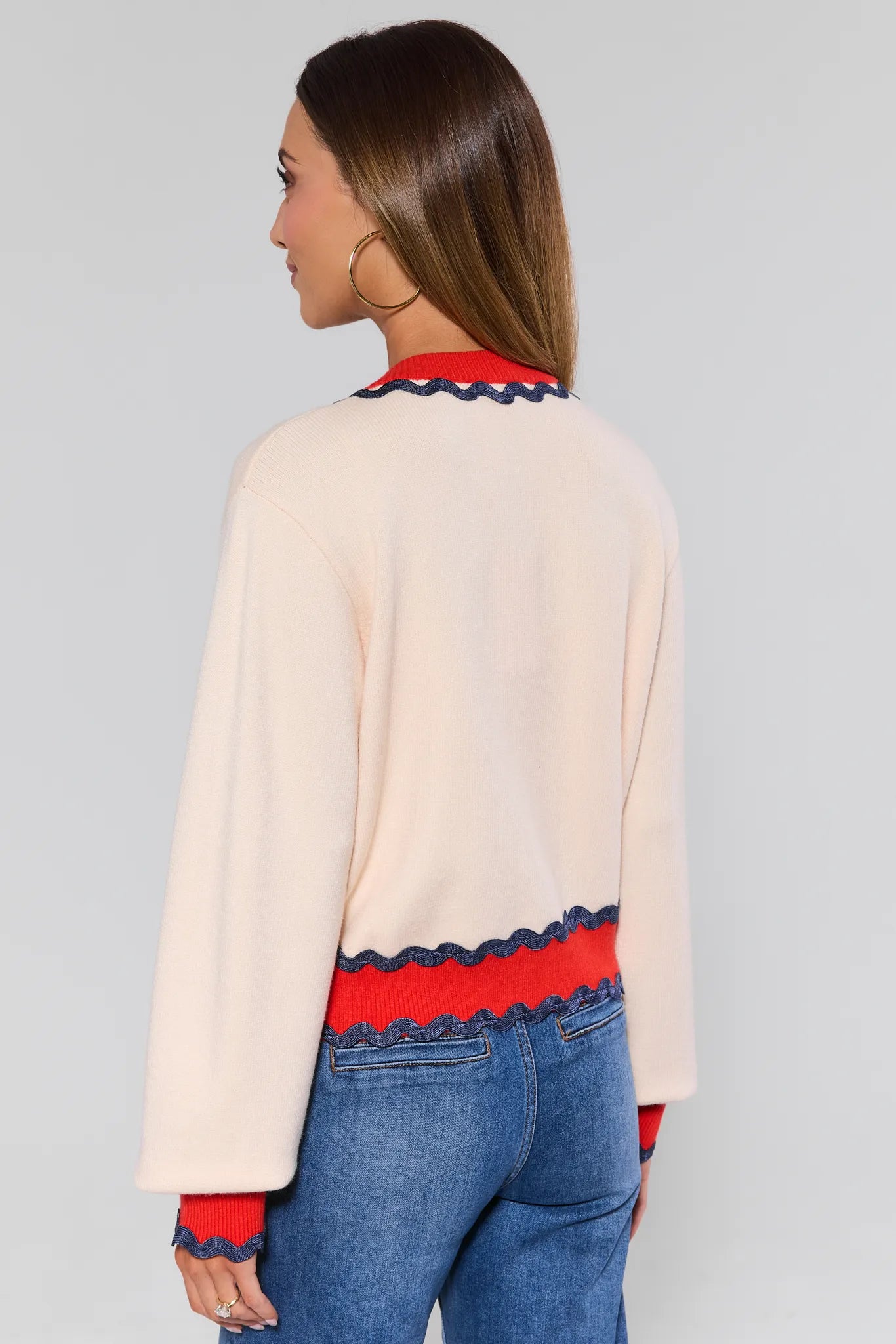 Woman wearing a beige sweater with red and blue accents and blue jeans on a gray background