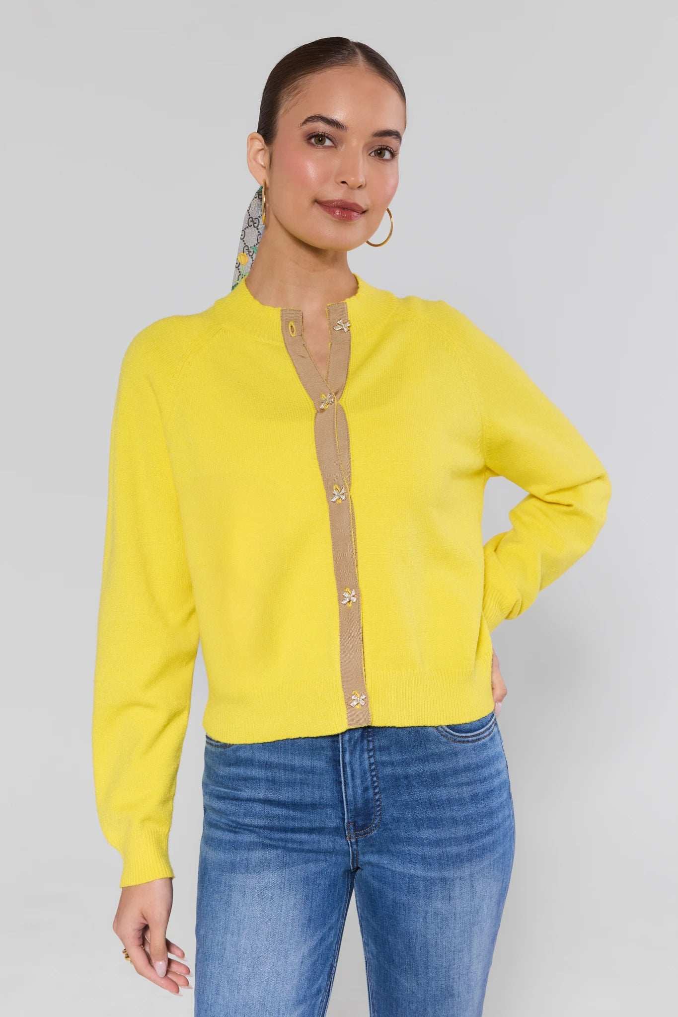 Woman wearing a yellow cardigan with a beige button-down shirt underneath, standing against a plain background.