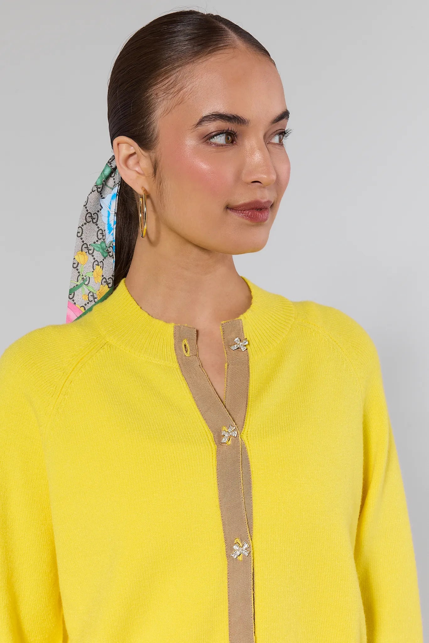 Woman wearing a yellow top with a decorative trim against a gray background