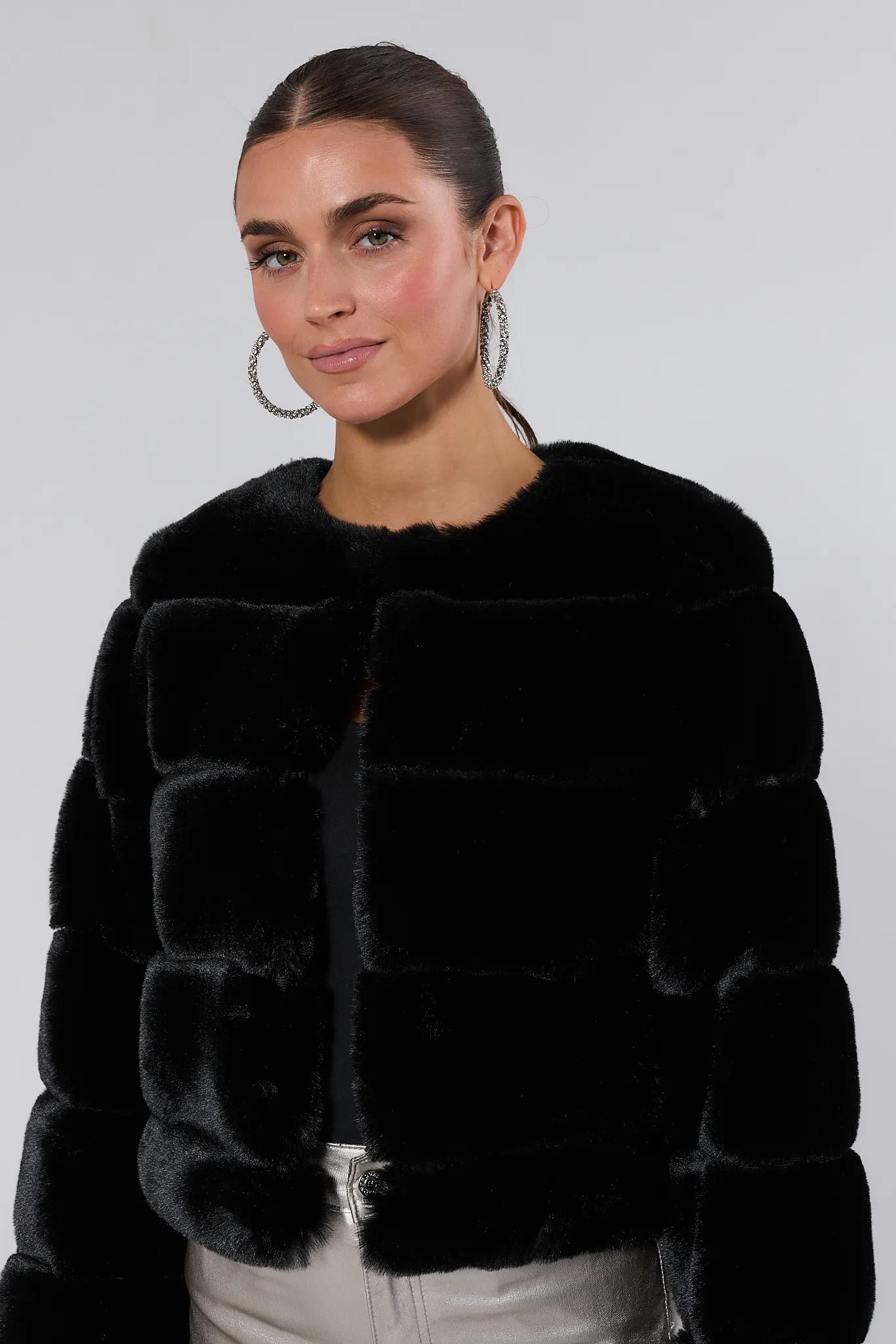 Woman wearing a Janet Black Faux Fur Jacket and silver pants on a white background