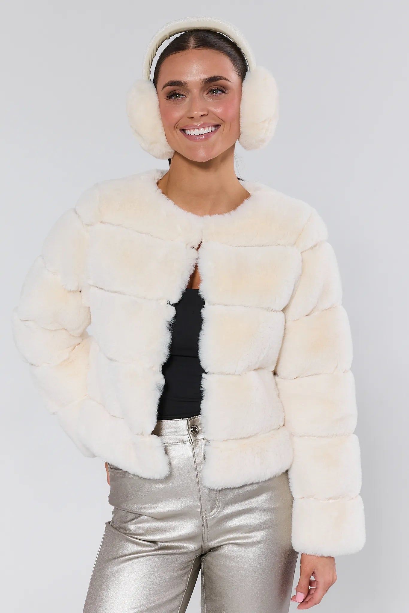Woman wearing a white fur coat and silver pants against a plain background