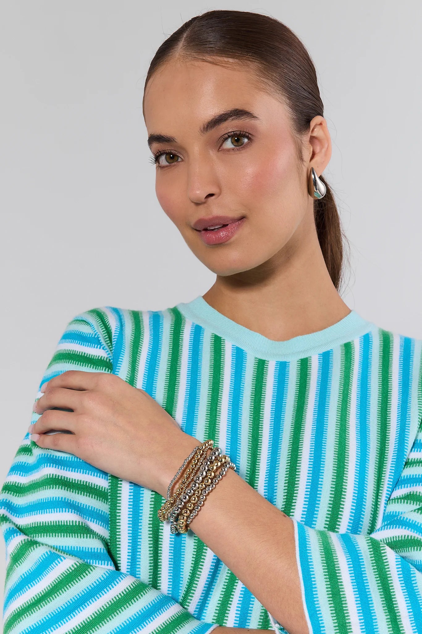 Woman wearing a striped sweater with bracelets on a plain background
