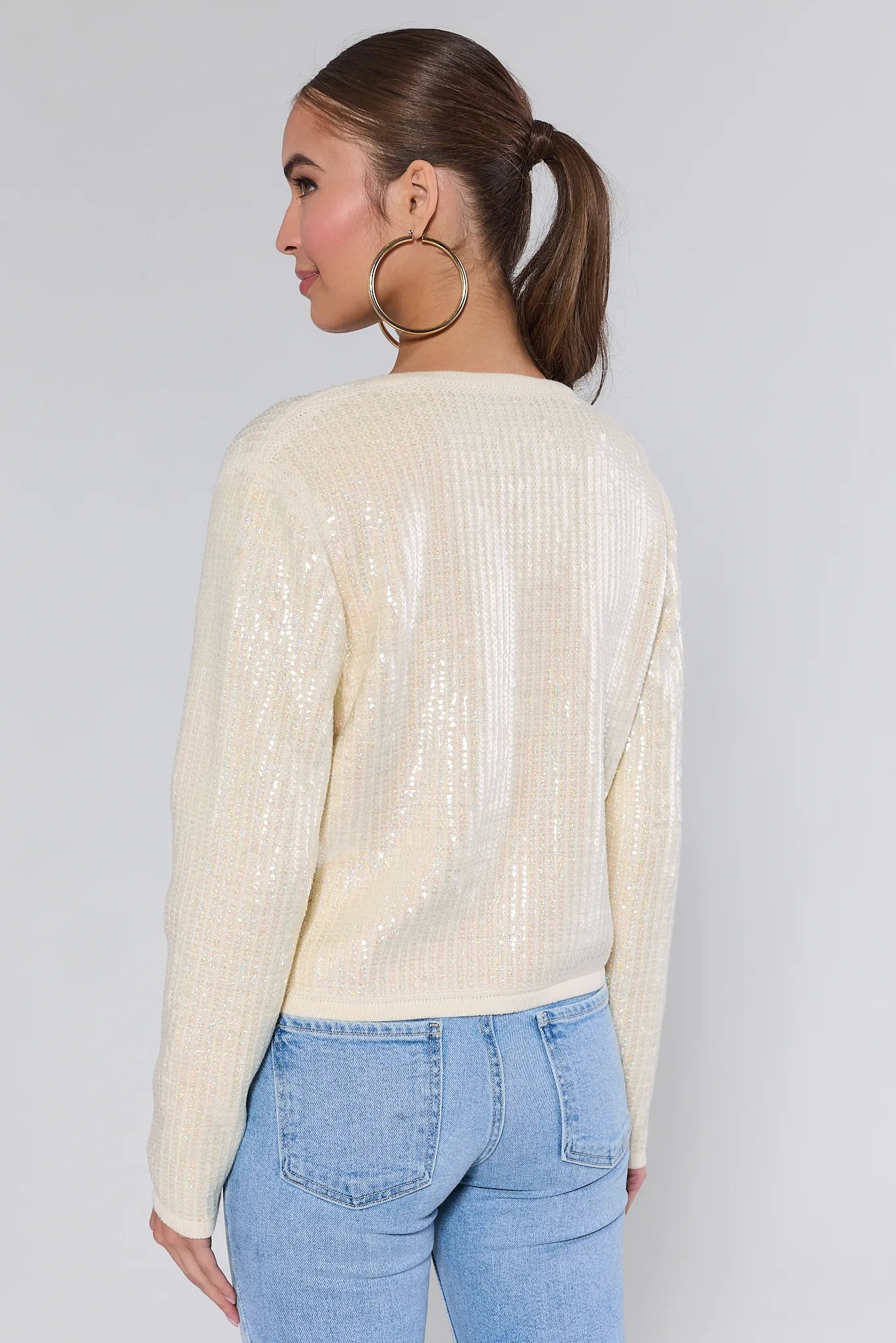 Woman wearing a cream libby cardigan over a white shirt and blue jeans on a plain background