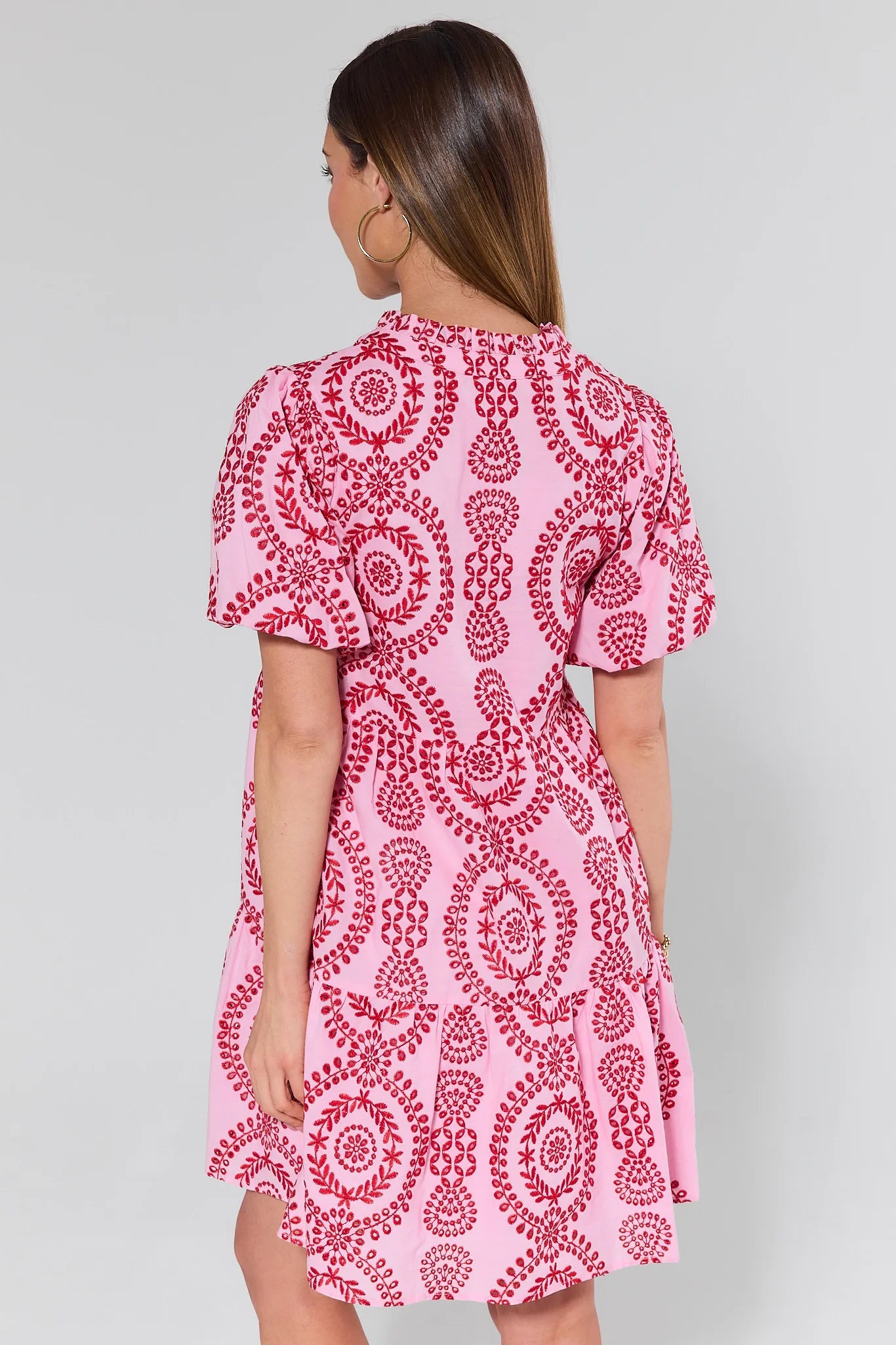 Woman standing backwards wearing a pink dress with red pattern on a gray background