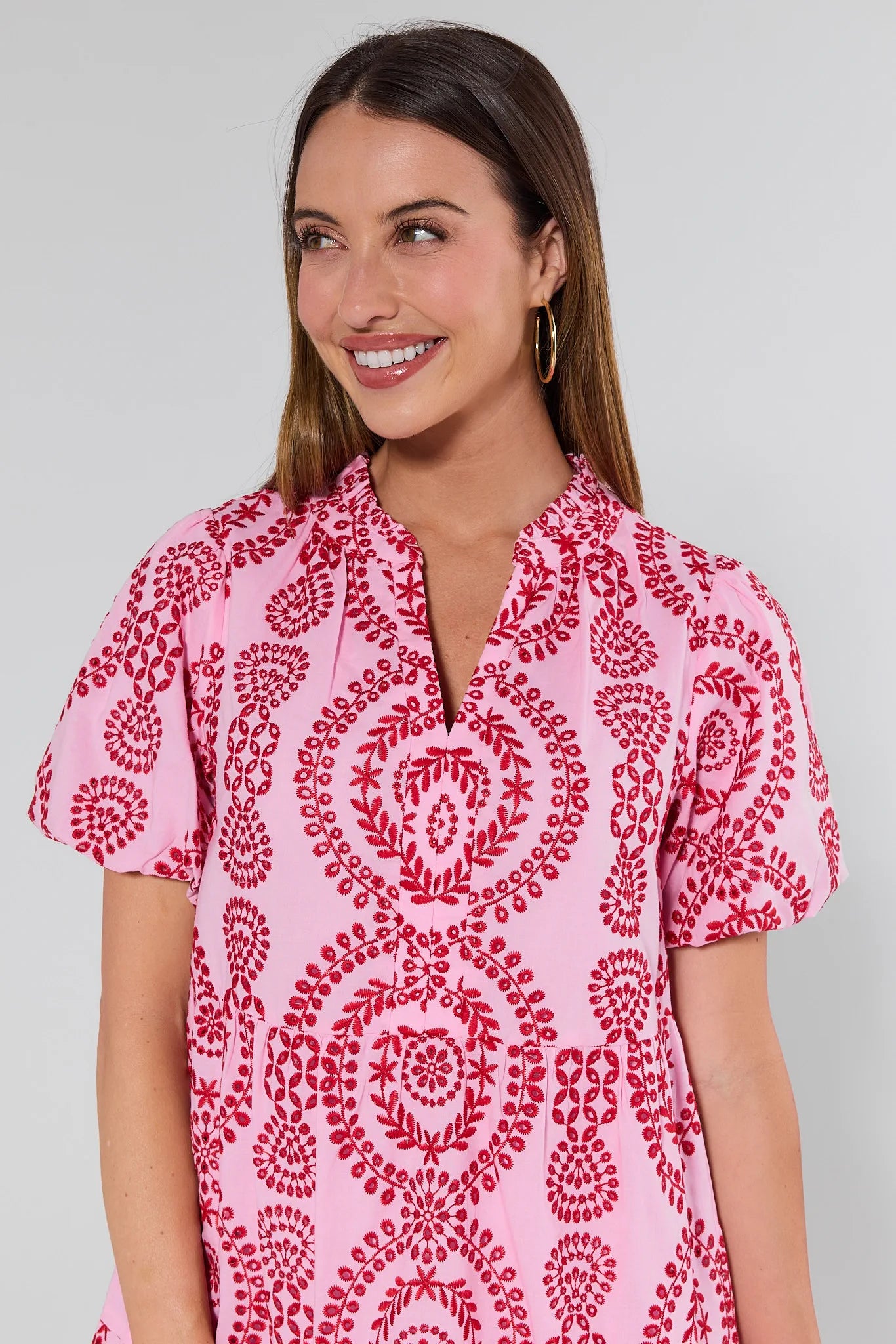 Woman wearing a pink dress with red pattern against a gray background