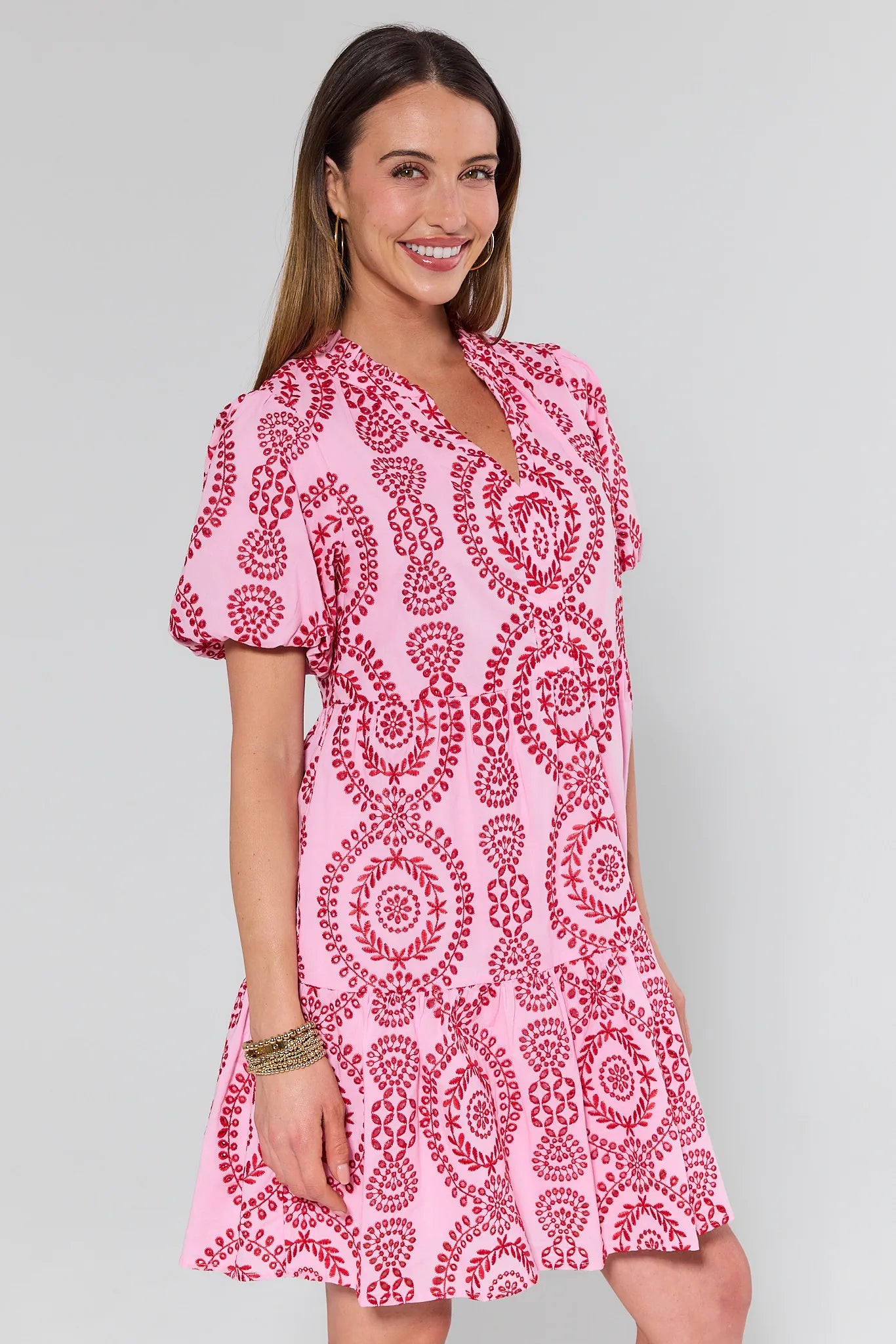 Woman standing at an angle wearing a pink and red patterned dress against a plain background