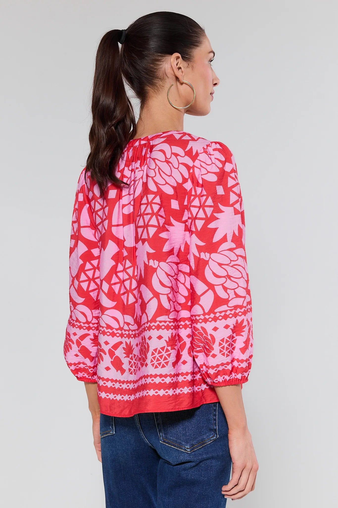 Woman wearing a pink and white patterned blouse on a plain background