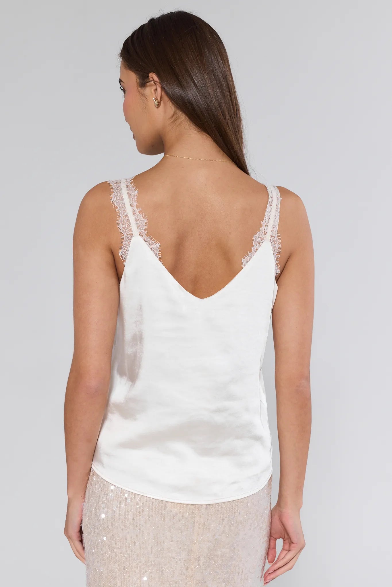 Woman wearing a white lace-trimmed tank top against a plain background