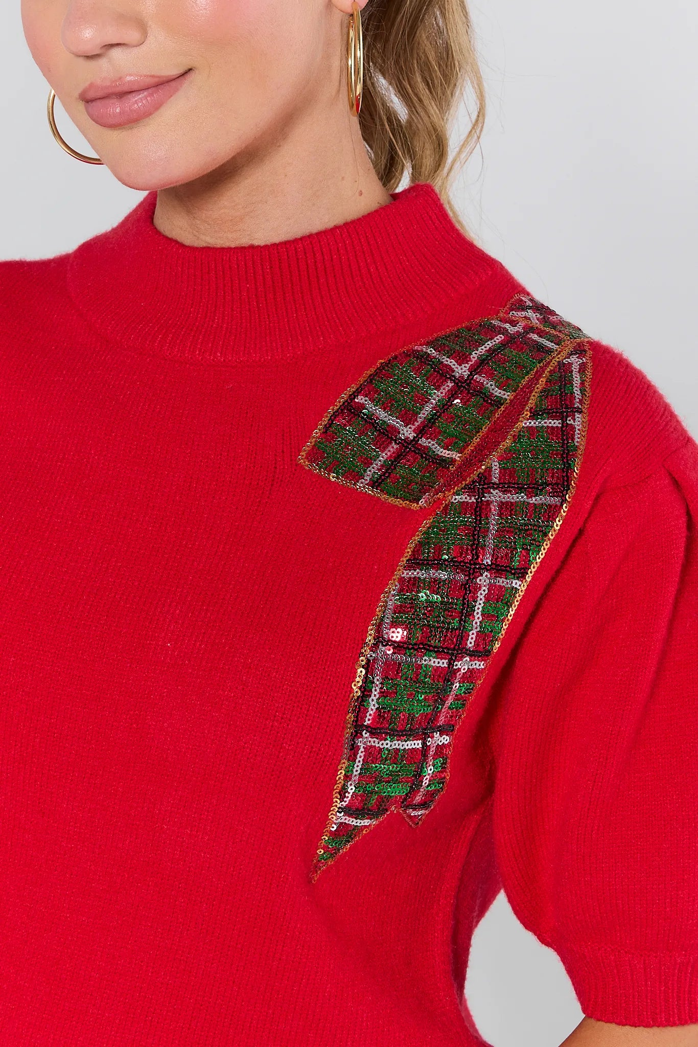 Woman wearing a Eve Red Sequin Bow Sweater on a plain background
