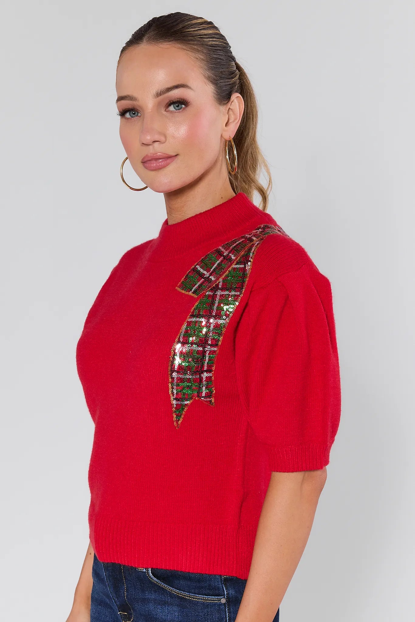 Woman wearing a Eve Red Sequin Bow Sweater on a plain background