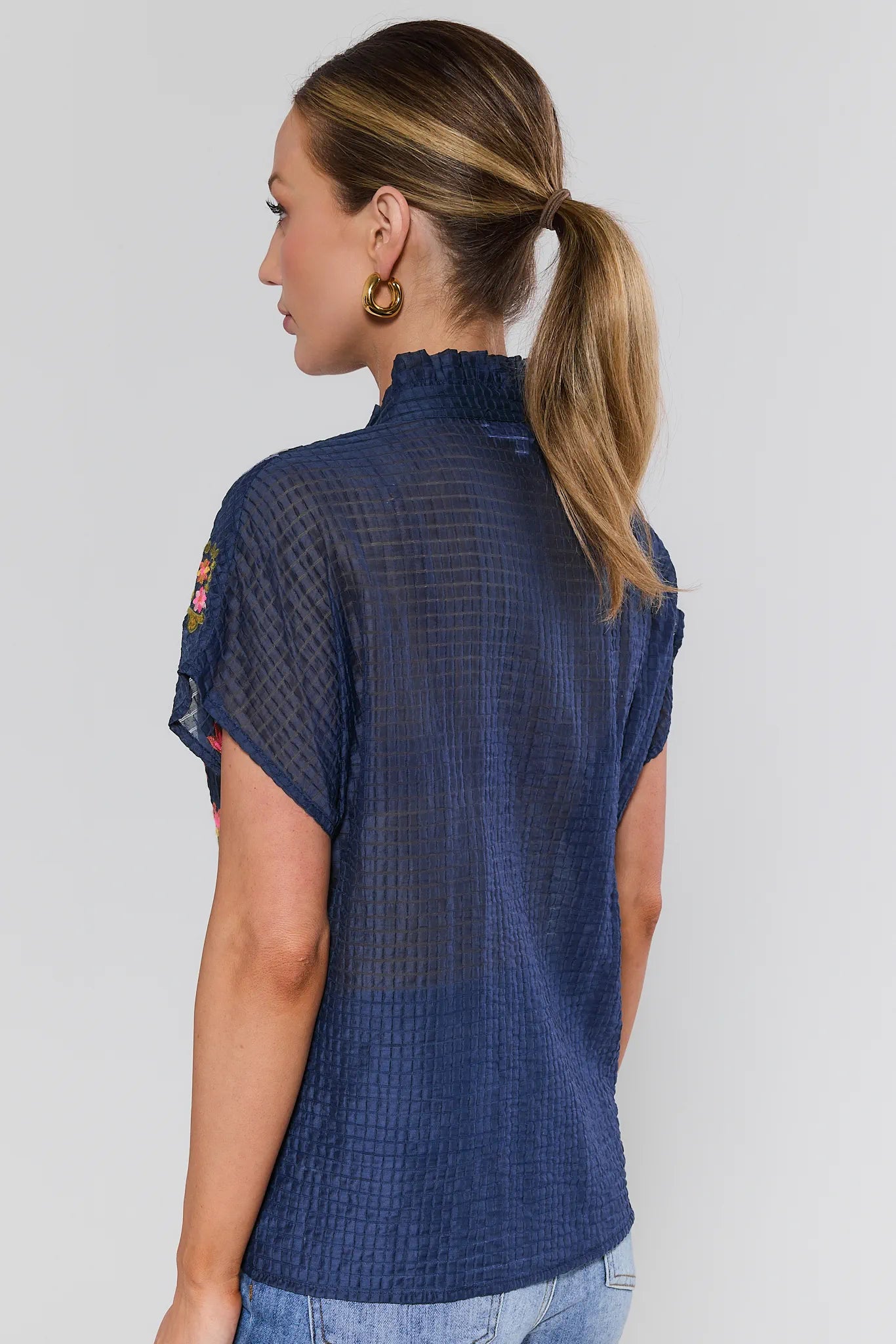 Woman wearing a blue textured top with short sleeves on a plain background