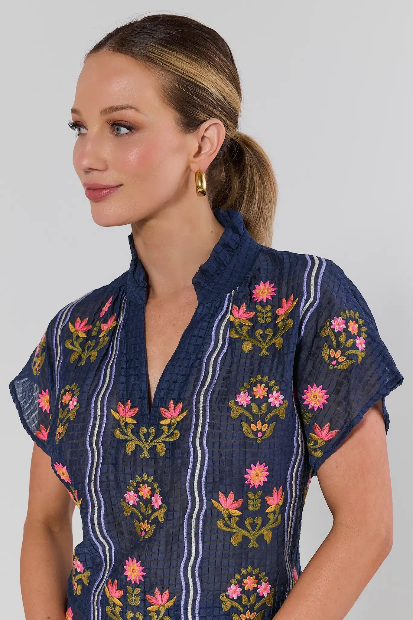 Woman wearing a navy blue embroidered blouse with floral patterns on a gray background