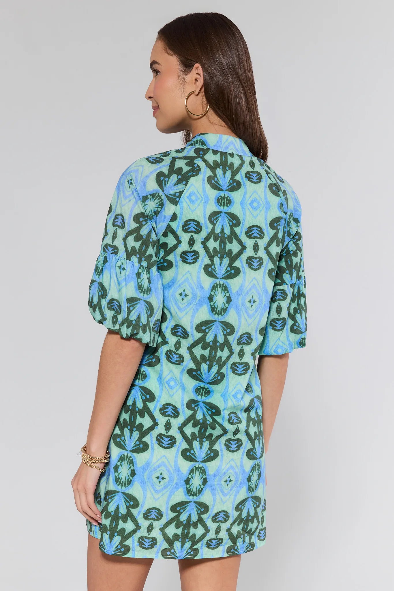 Woman wearing a green and blue patterned dress on a plain background