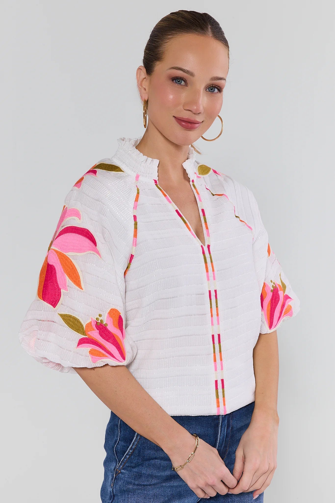Woman wearing a white blouse with colorful floral patterns on a plain background