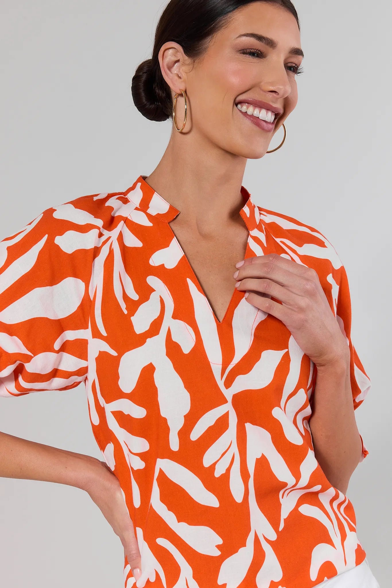 close up Woman wearing an orange and white patterned blouse against a plain background