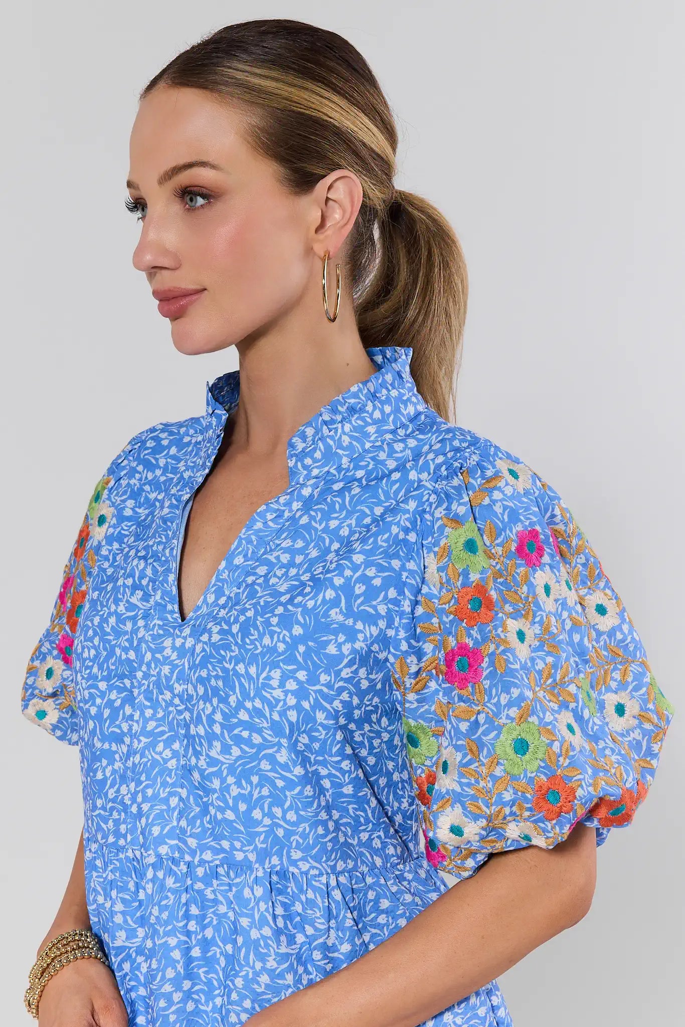 Woman wearing a blue floral dress with colorful sleeves against a plain background