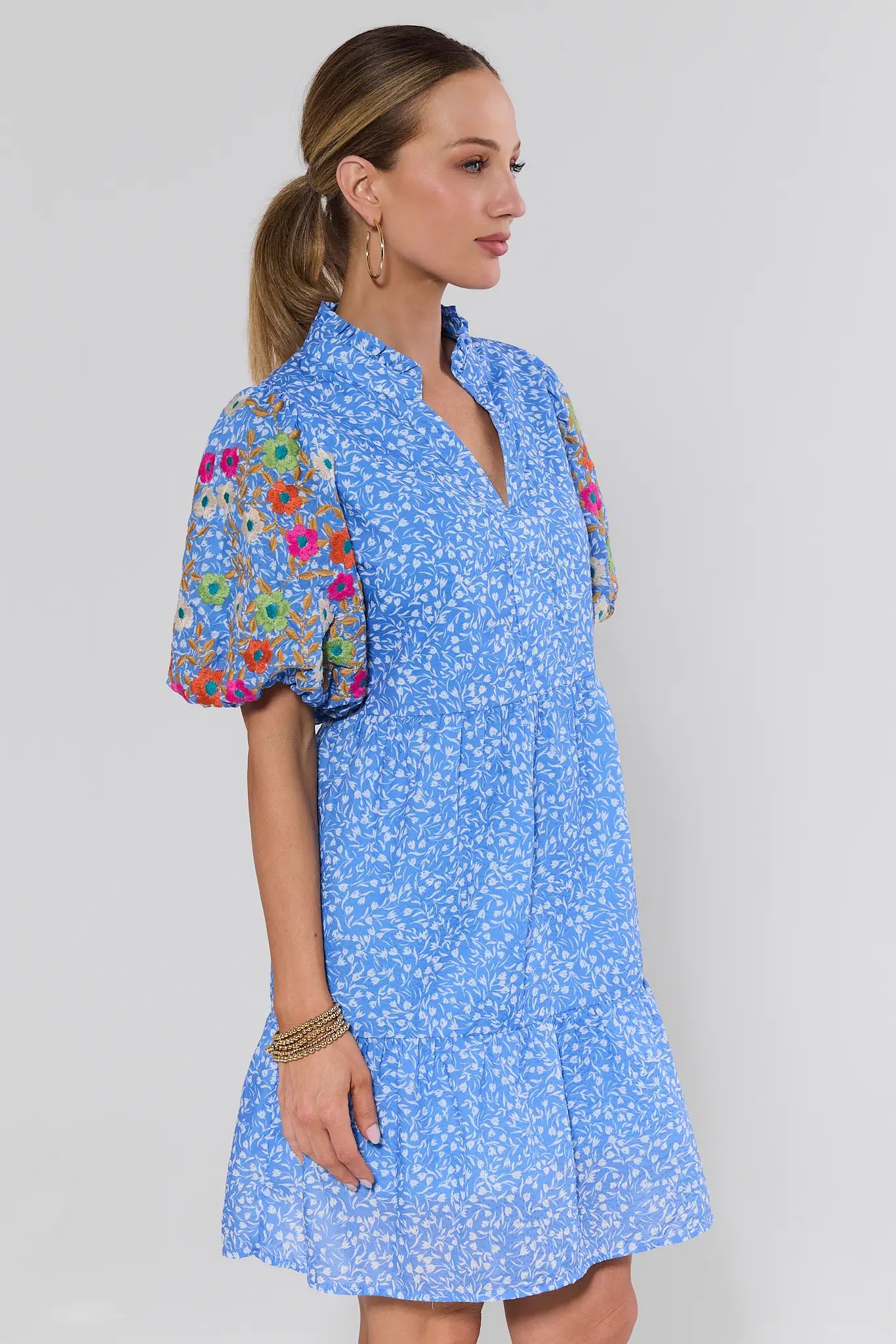Model in profile wearing the Sue Ann Blue Floral Short Dress by THML, featuring a shift silhouette, puffed sleeves with floral embroidery, and a flounce hemline.
