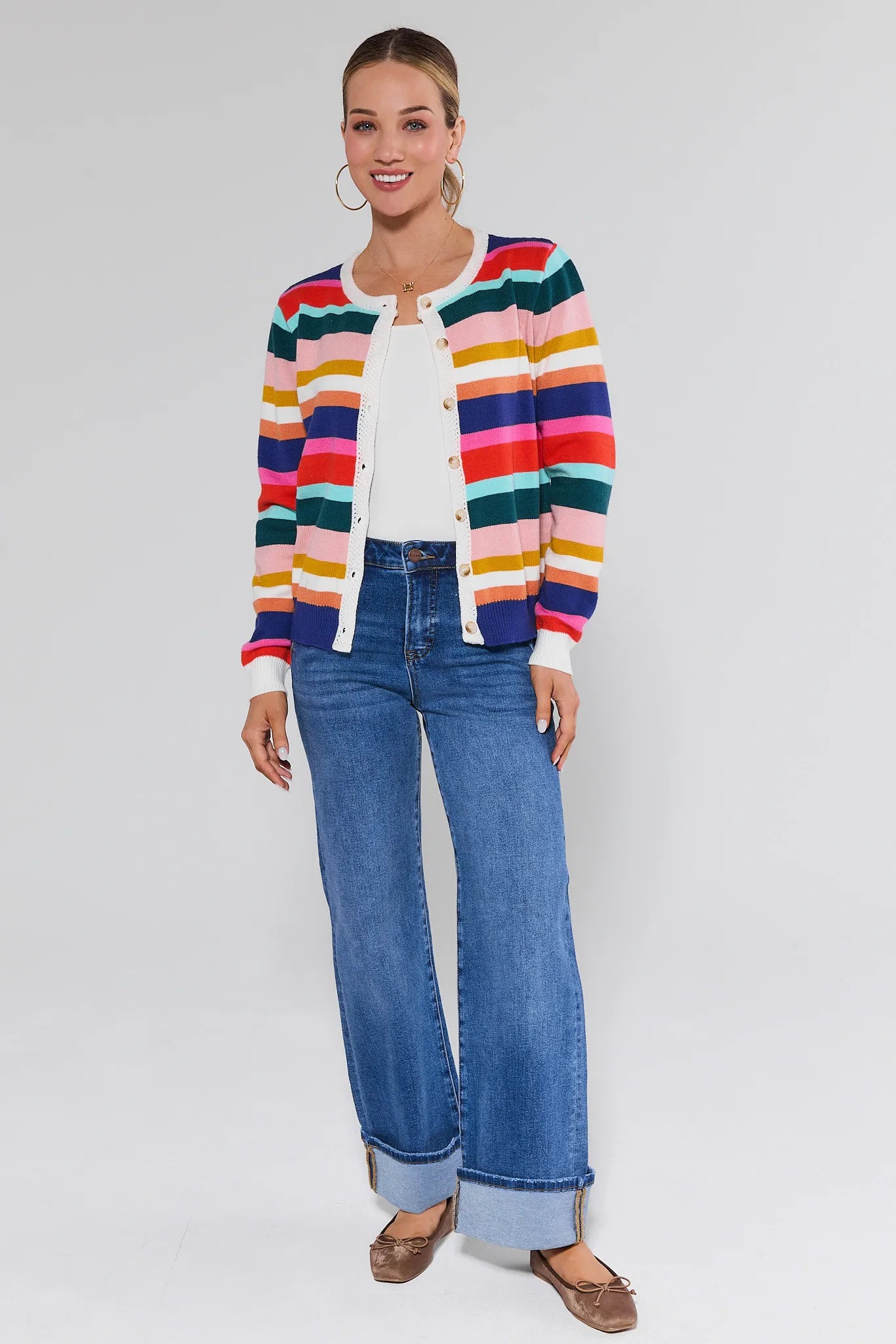Woman wearing a colorful striped cardigan and blue jeans on a white background
