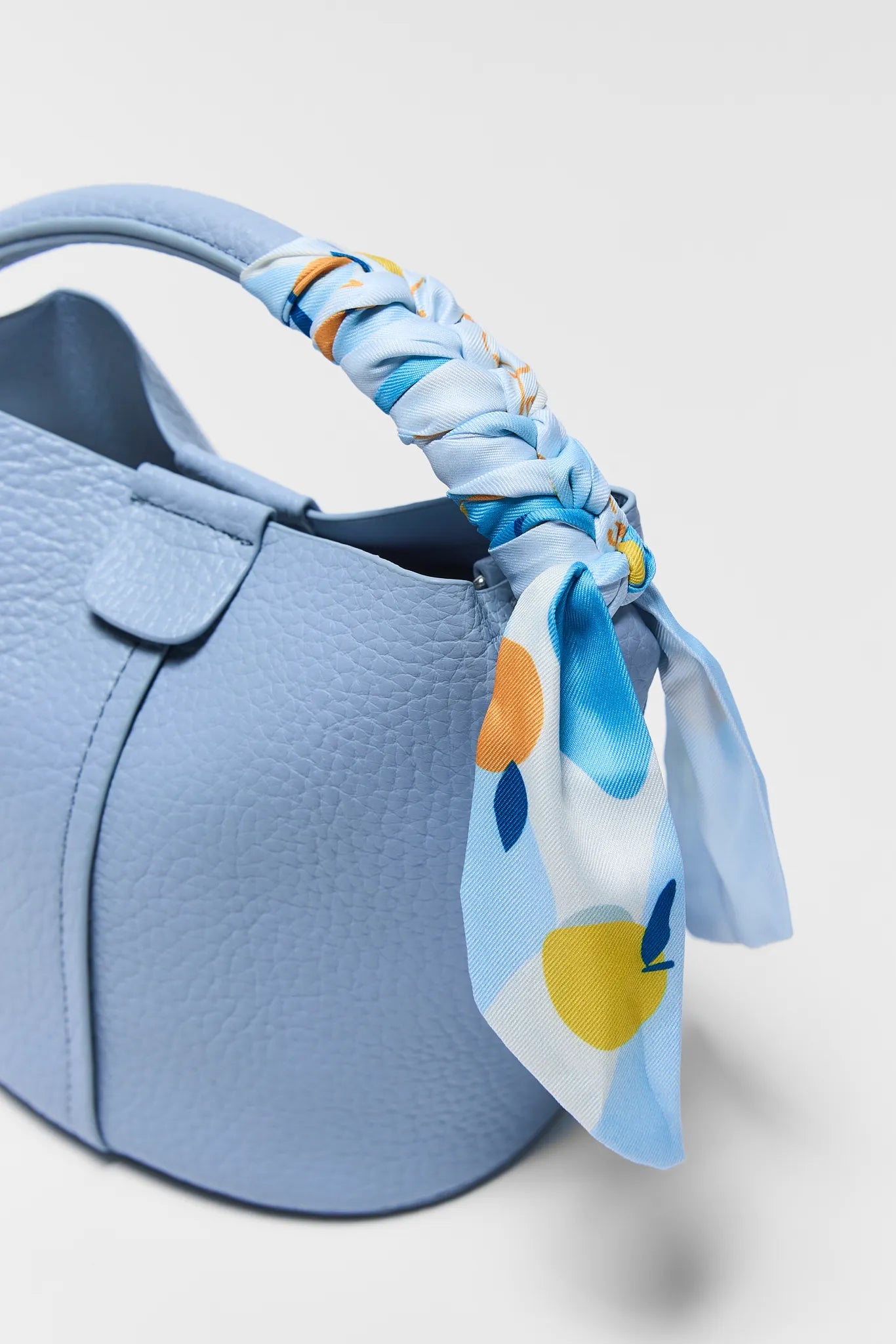 Blue handbag with a floral scarf on a light gray background