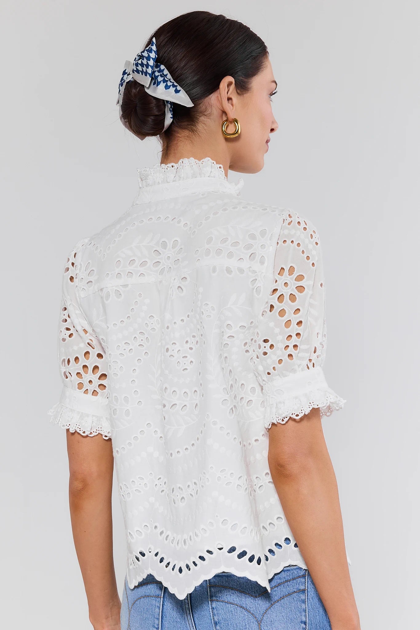 Woman wearing a white lace top with blue jeans and hair scarf on a plain background