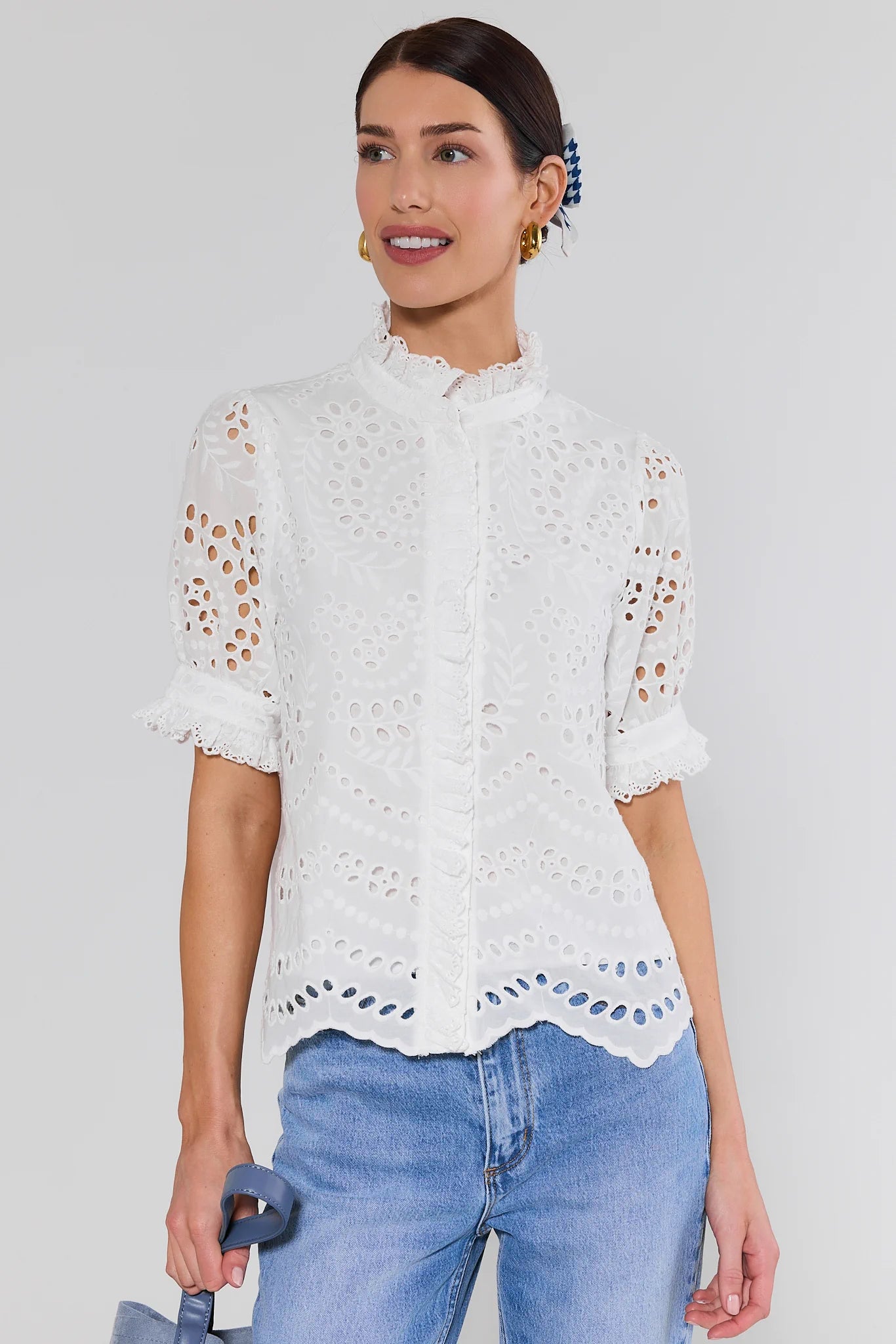 Woman wearing a white lace blouse and blue jeans against a plain background