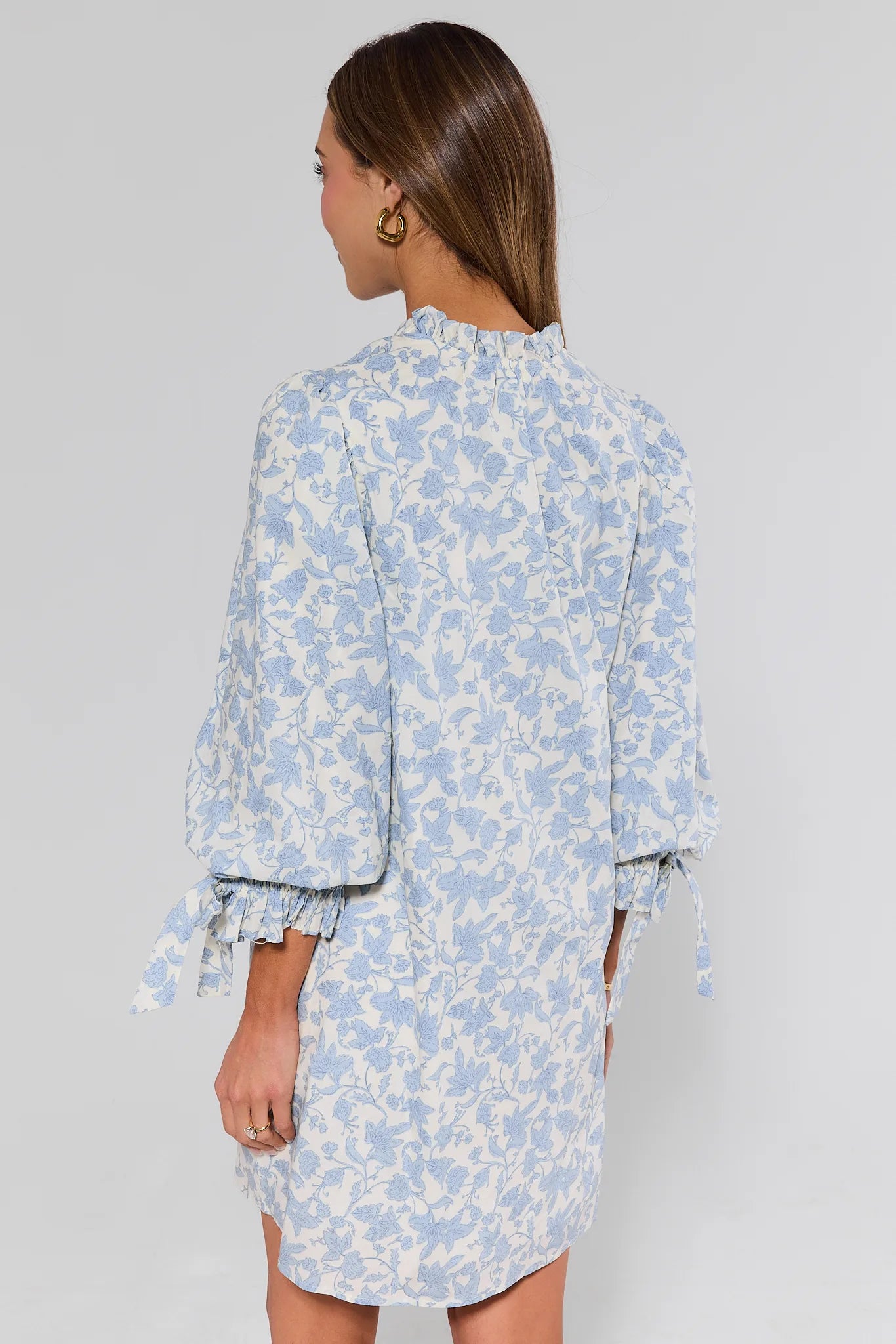 Woman standing wearing a blue floral dress against a gray background