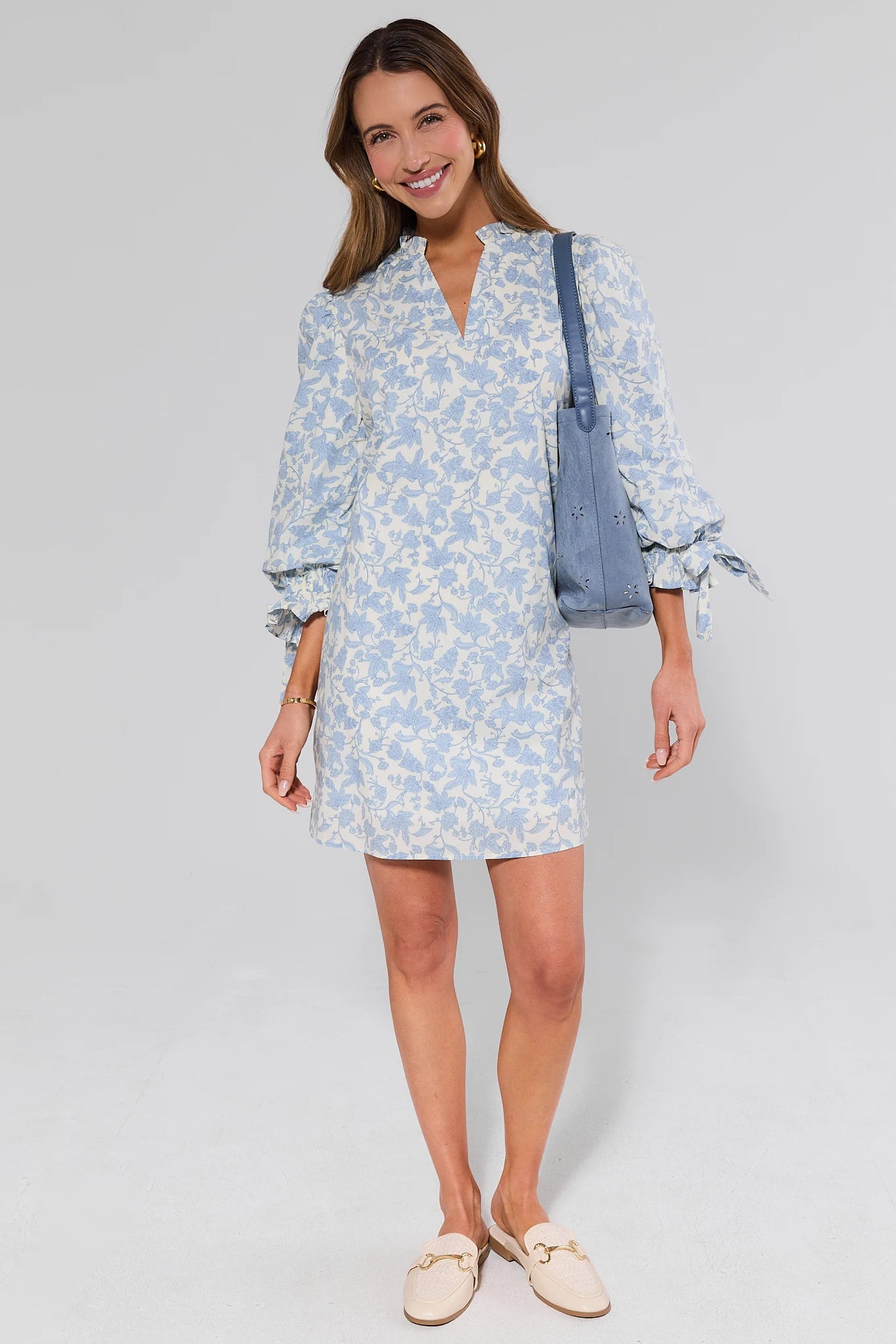 Woman wearing a light blue floral dress with a suede bag on a white background