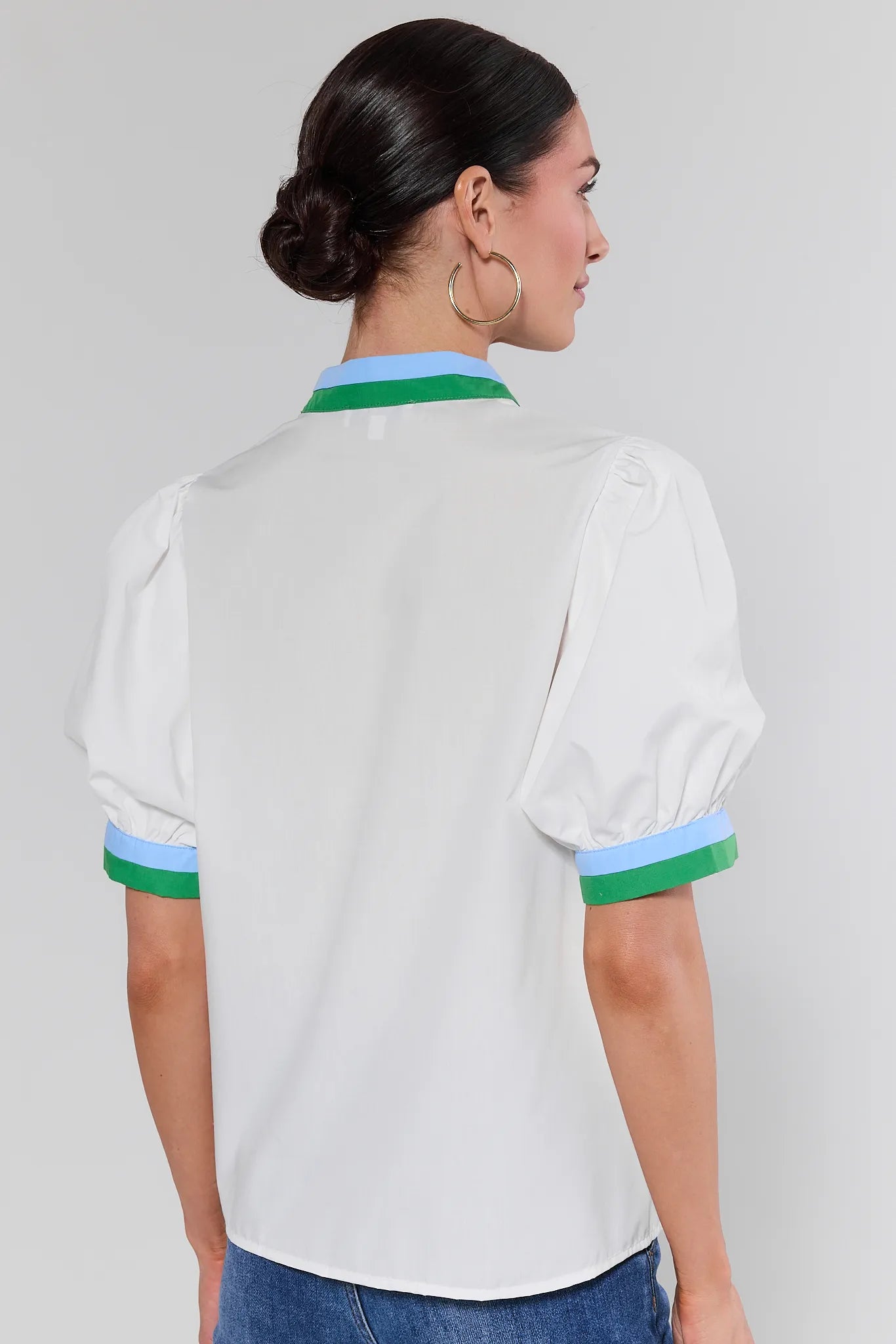 Woman wearing a white blouse with green and blue trim on a plain background