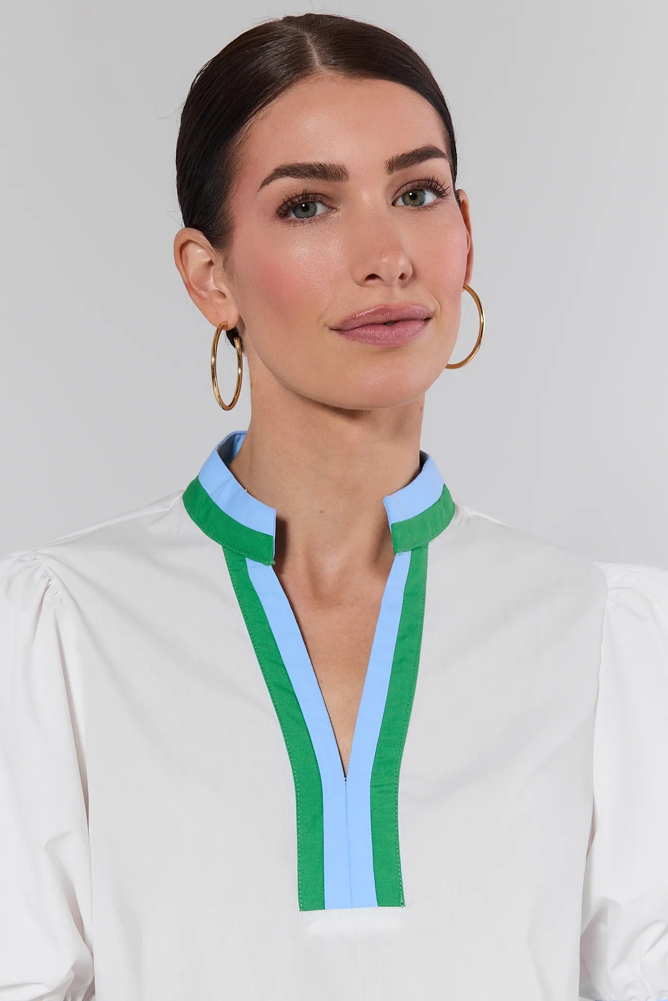 Woman wearing a white blouse with green and blue accents on a plain background