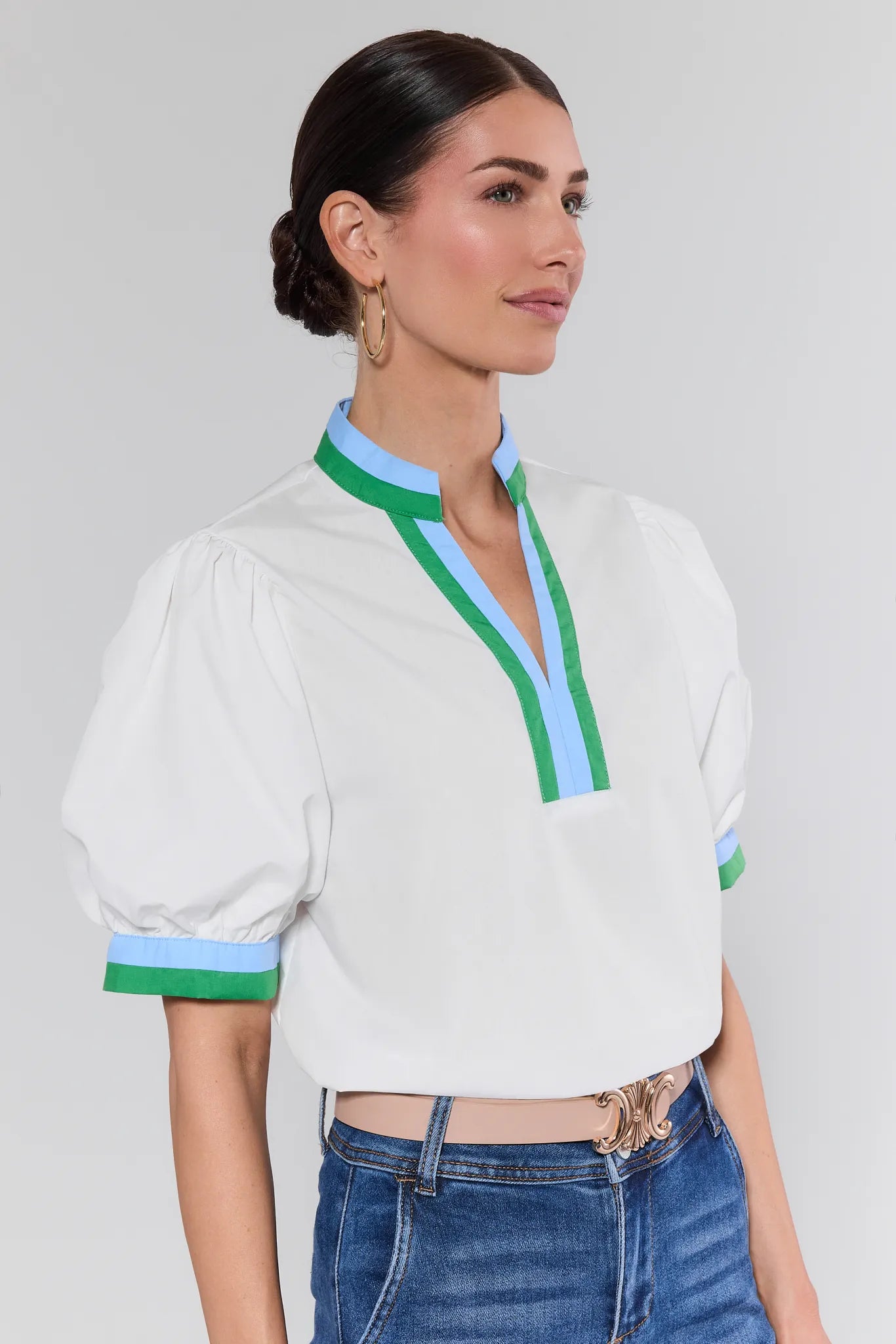 Woman wearing a white blouse with green and blue accents on a plain background