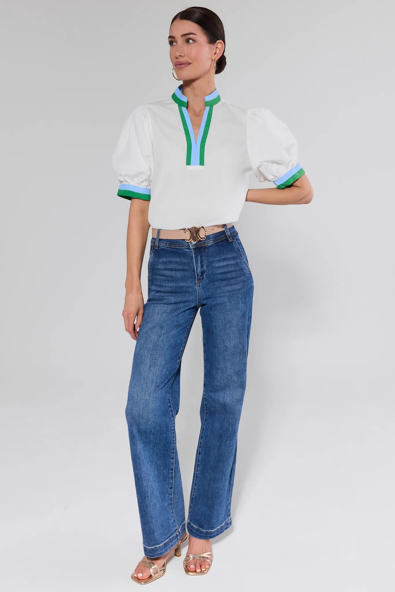 Woman wearing a white blouse with colorful accents and blue jeans on a plain background