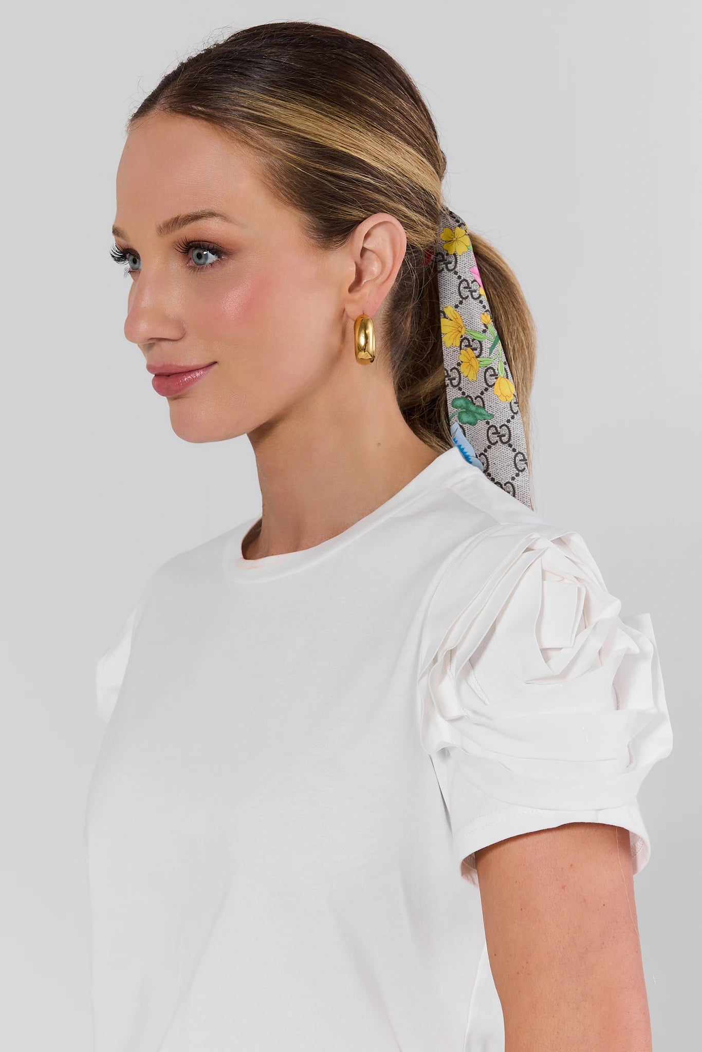 Woman wearing a colorful hair scarf with a white top on a light gray background