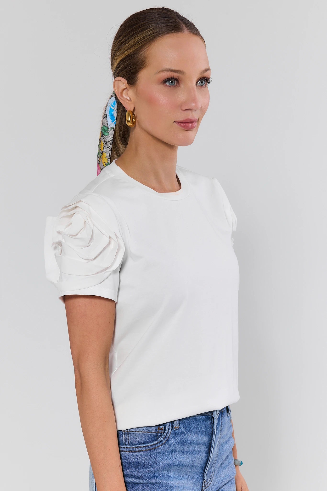 Woman wearing a white top with ruffled sleeves and blue jeans against a light gray background