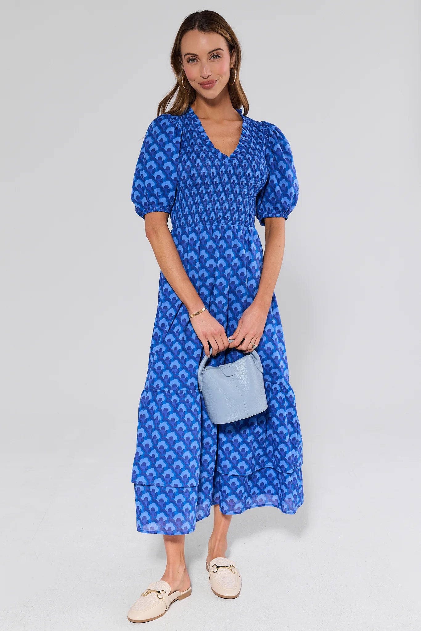 Woman wearing a blue patterned dress holding a matching handbag against a white background