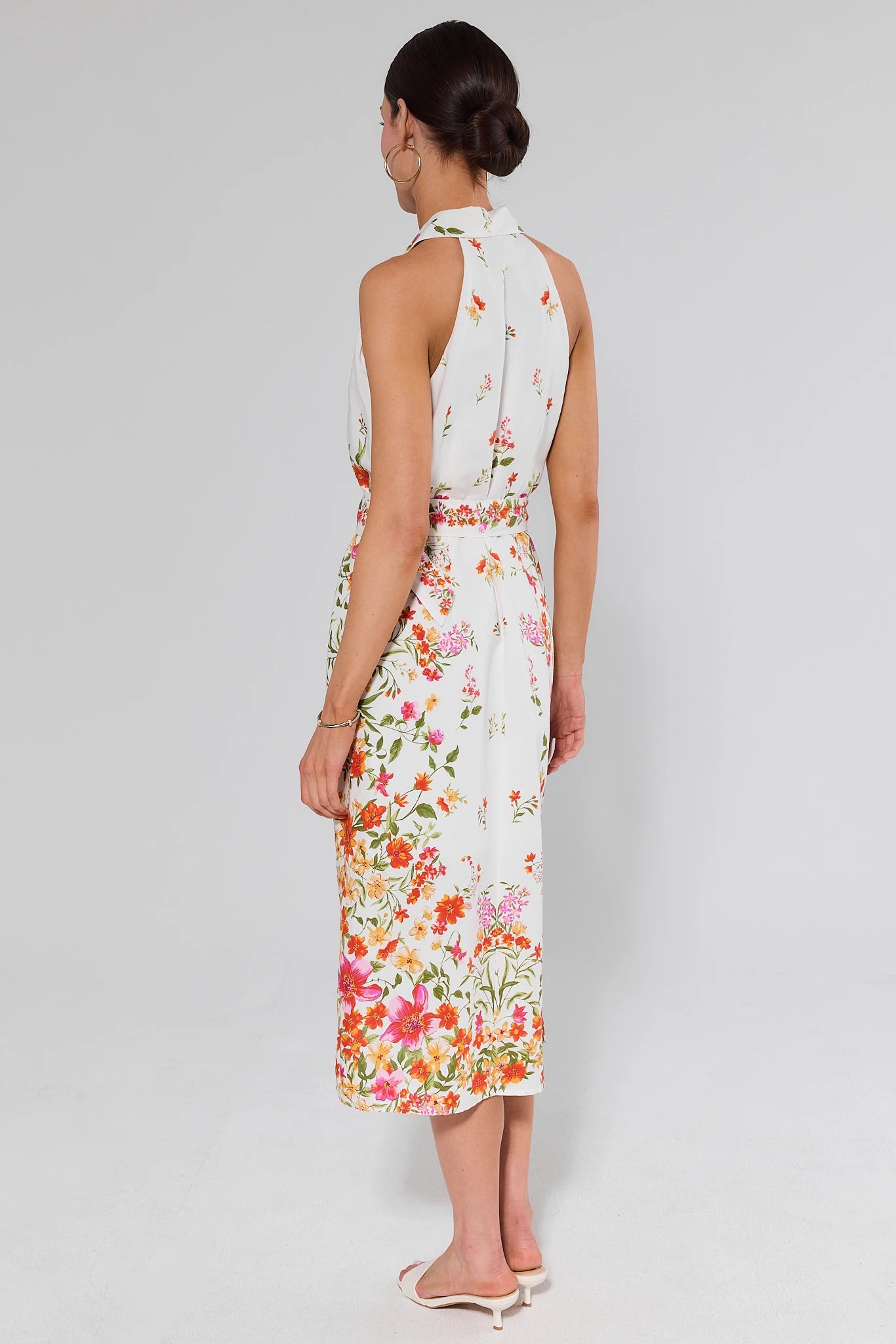 Woman standing wearing a floral dress on a plain background