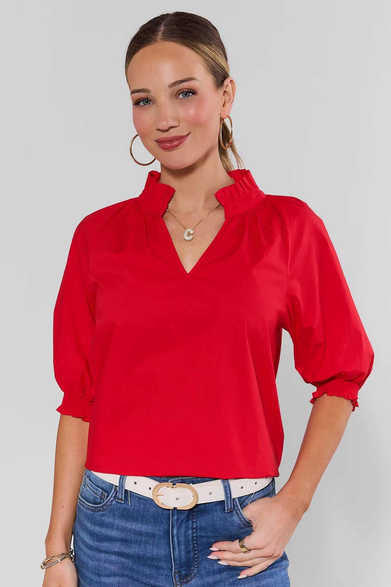 Woman wearing a red blouse and blue jeans against a gray background