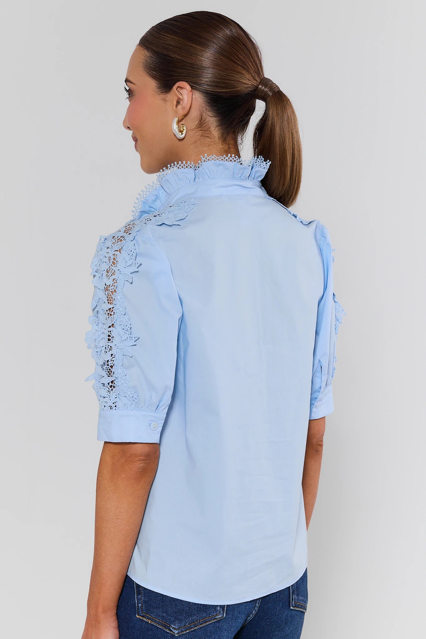 Woman wearing a light blue denim shirt with decorative sleeves on a plain background