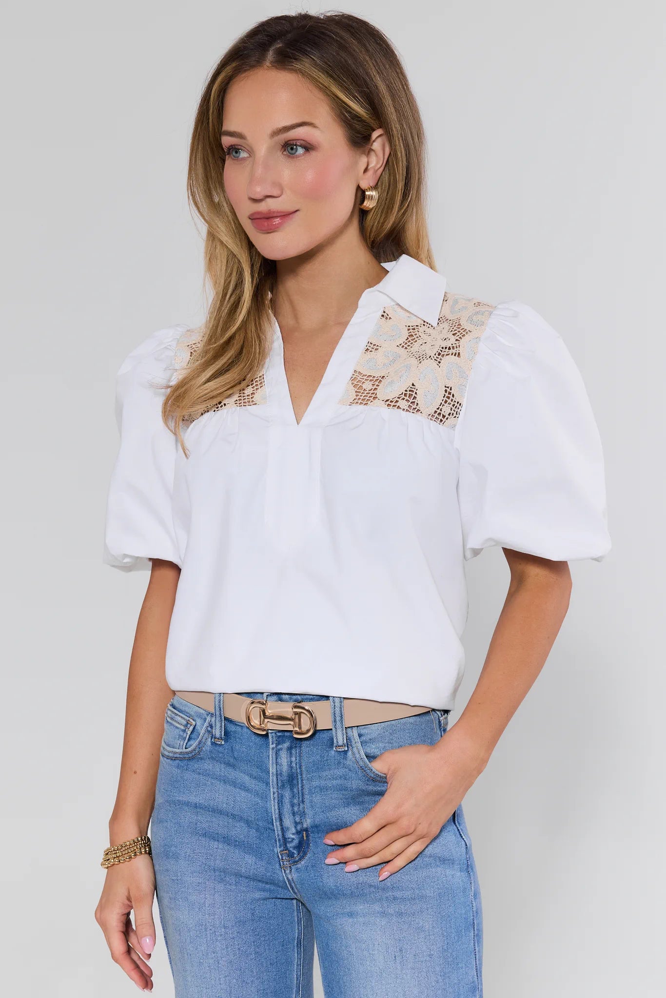 Woman wearing a white blouse with floral embroidery and blue jeans on a plain background