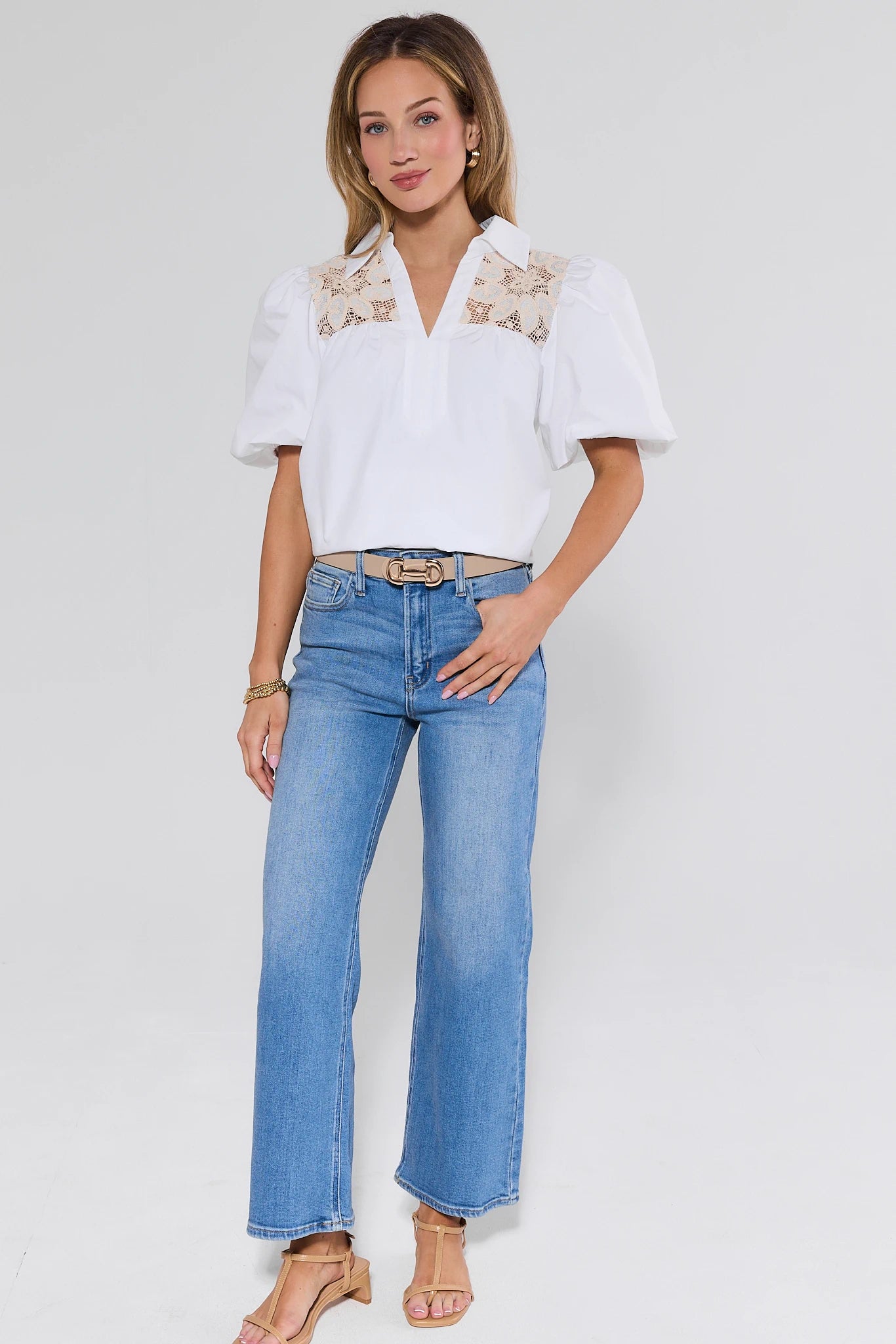 Woman wearing a white blouse with lace details and blue jeans on a plain background