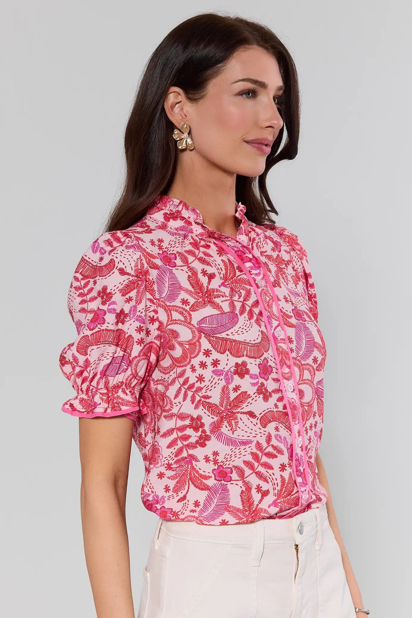 side shot Woman wearing a pink floral blouse against a gray background