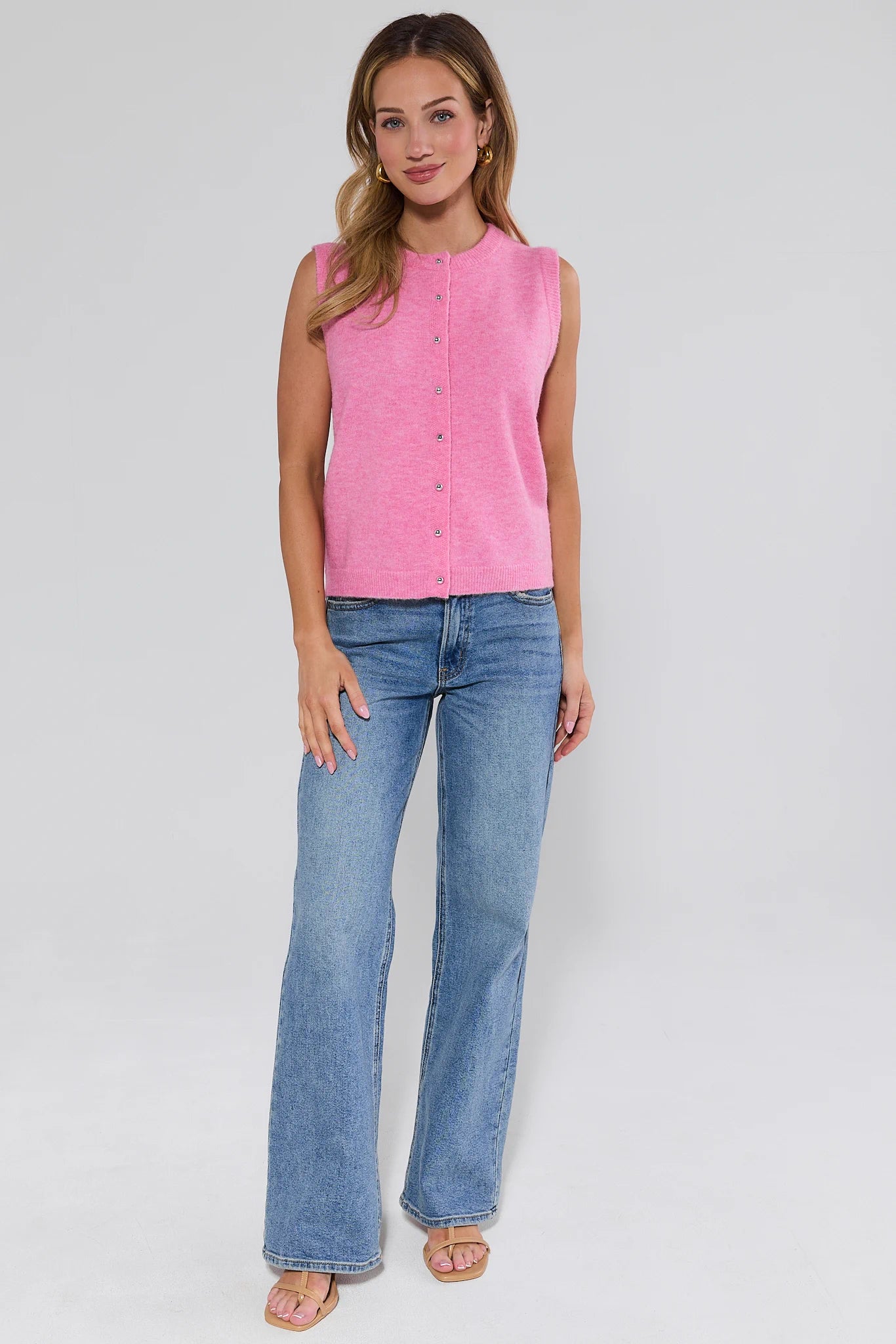 Woman wearing a pink sleeveless top and blue jeans on a white background