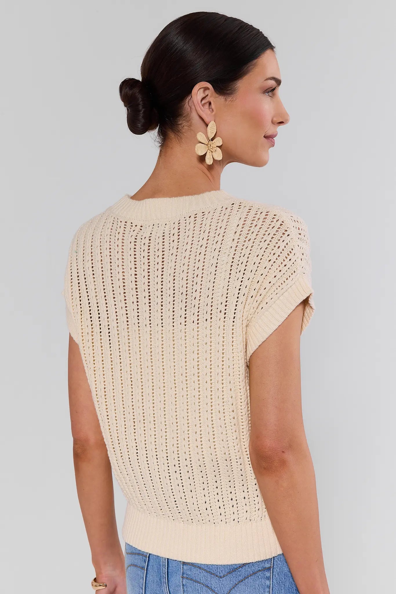 Woman standing wearing a beige knitted top with a plain background