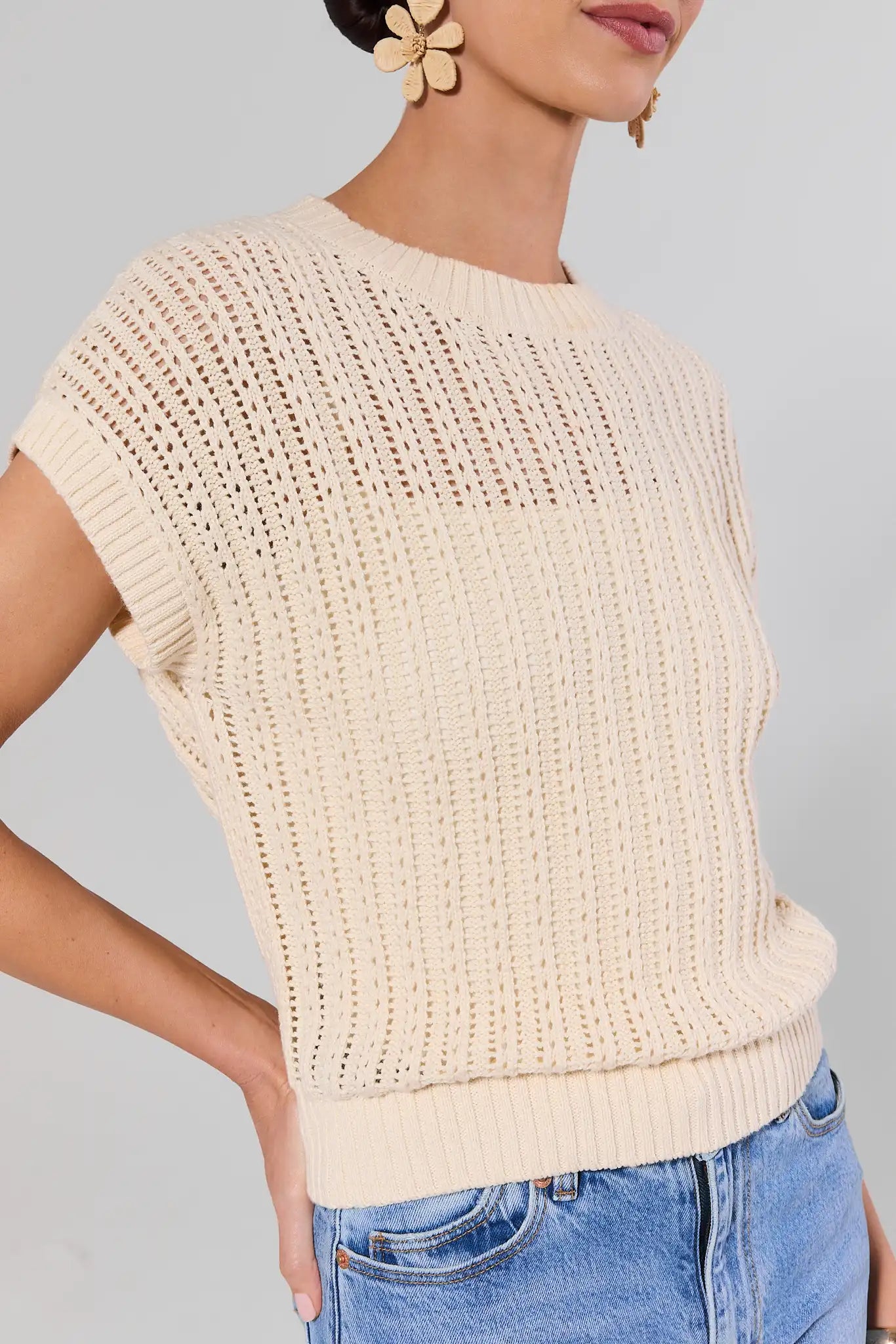 close up Woman wearing a beige knitted top and blue jeans against a gray background