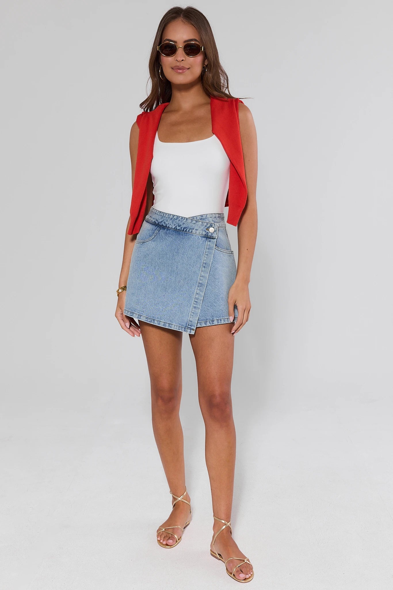 Woman wearing a red jacket, white top, and denim skirt on a plain background