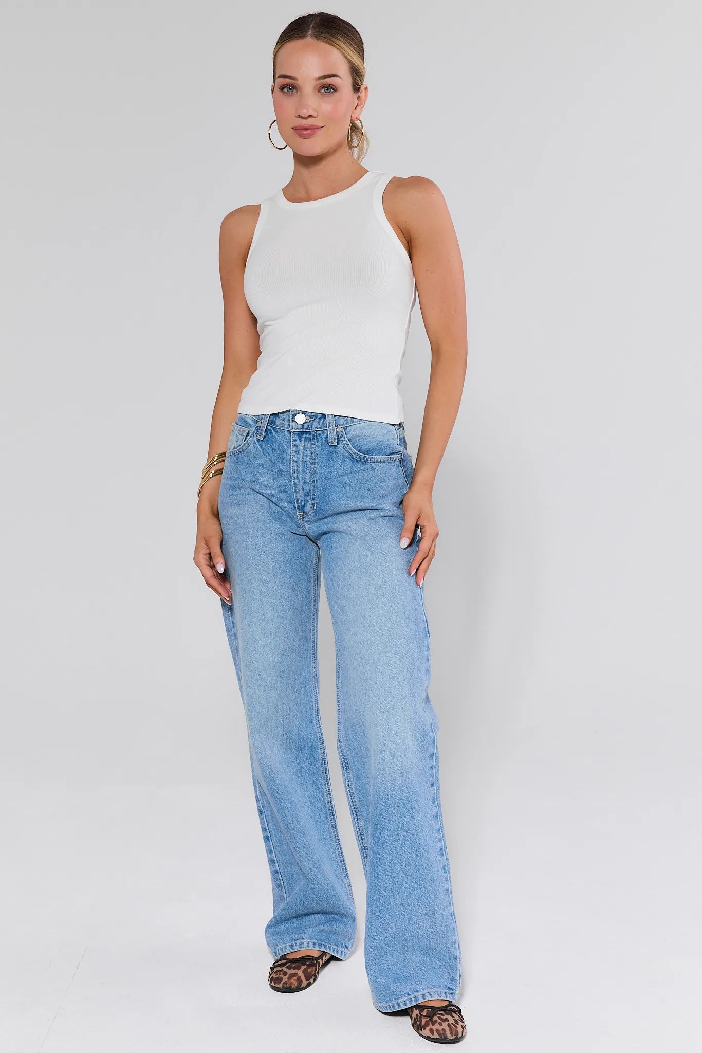 Woman wearing a white sleeveless top and light blue jeans on a plain background