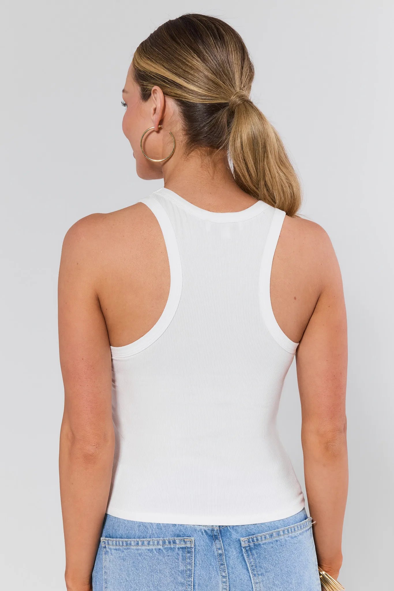 Woman wearing a white allie tank top against a plain background